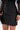 A close-up of someone wearing the THIS IS THE LIFE FAUX LEATHER MINI SKIRT with horizontal ribbed lines, paired with a sheer black lace top and a small feather-detailed black clutch.