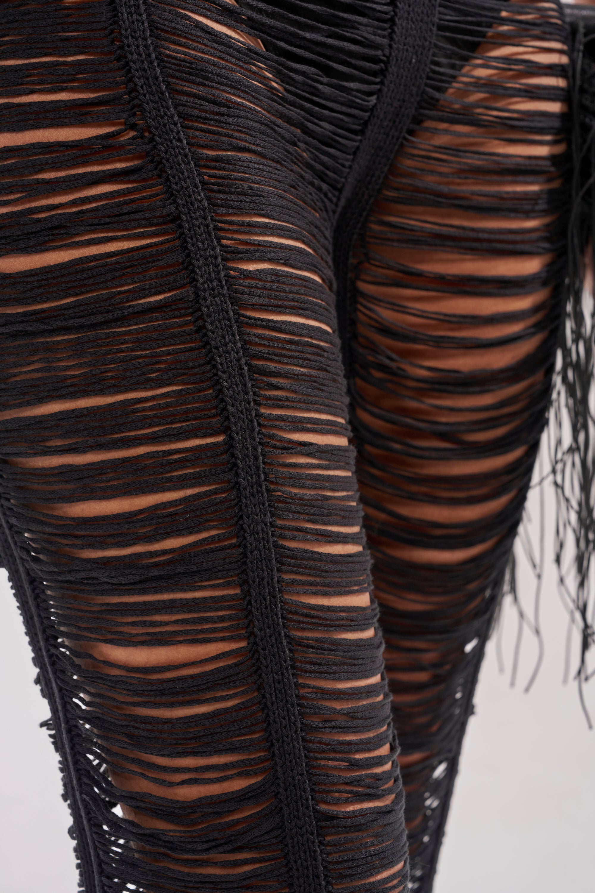 Close-up of the IT GIRL SHREDDED JUMPSUIT featuring black pants with multiple horizontal slits that reveal skin beneath, giving the distressed fabric a bold and edgy texture. 6