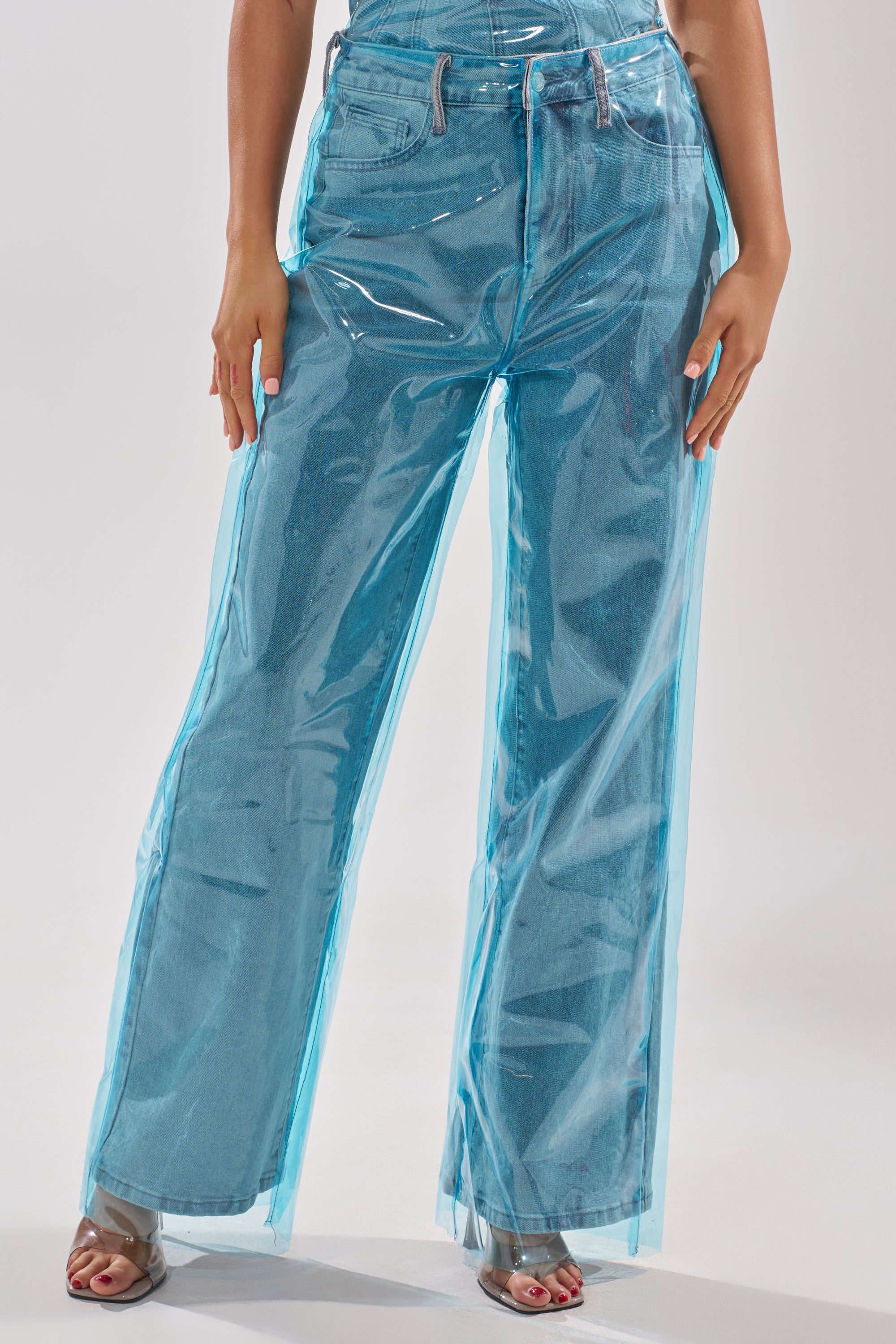 A person wears ELECTRIC FEEL WIDE LEG DENIM featuring a blue PVC overlay, styled with open-toed shoes. The image is cropped from waist to feet. 1