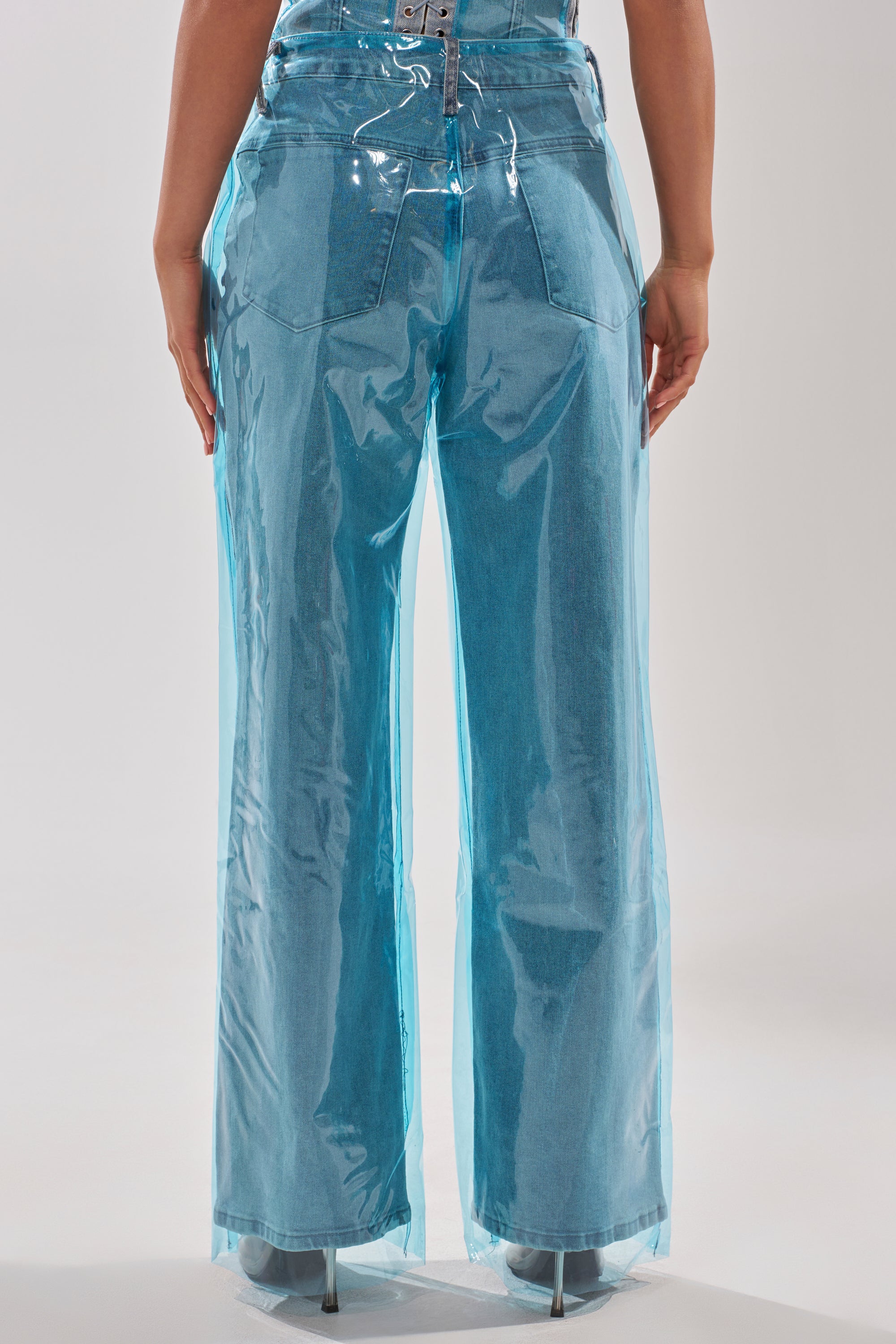 A person is shown from the back wearing ELECTRIC FEEL WIDE LEG DENIM—high-rise, wide-leg jeans with a shiny blue PVC overlay—paired with clear-heeled shoes for a modern, stylish look. 4