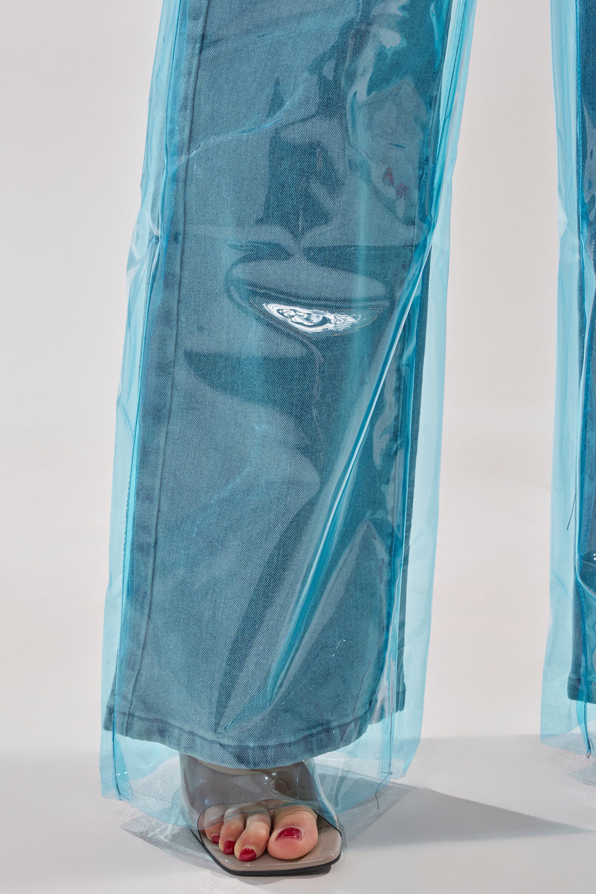 A close-up of ELECTRIC FEEL WIDE LEG DENIM features blue-tinted PVC overlay and partially visible feet in clear heeled sandals with red nail polish. 7