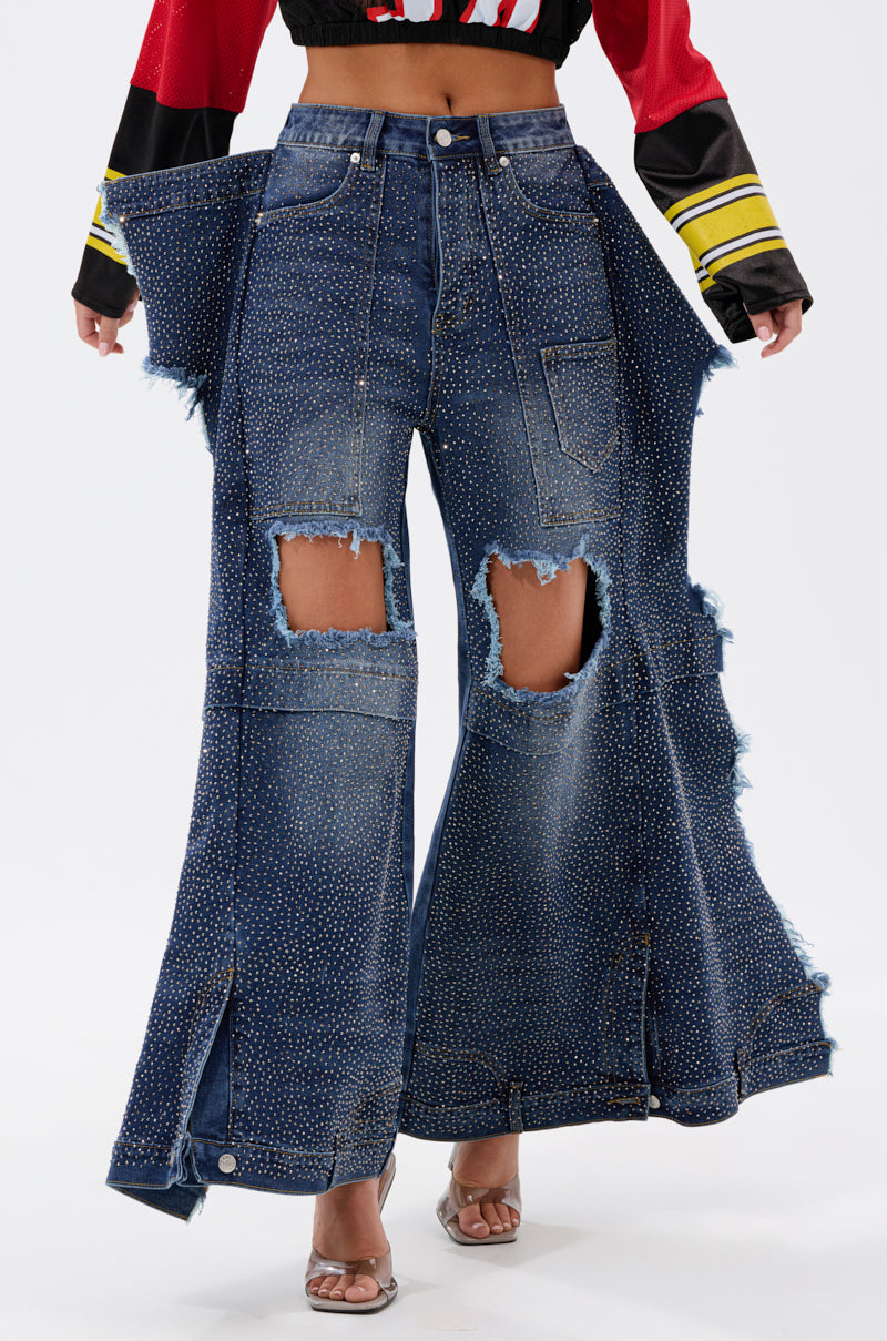 Wearing SPARKLE QUEEN WIDE-LEG DENIM with rhinestone accents, large front rips, and bold side panels, styled with heeled sandals and a cropped long-sleeve top for a striking statement look.