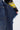 A person in a black and yellow striped sleeve holds the SPARKLE QUEEN WIDE-LEG DENIM, blue jeans adorned with small silver studs and frayed edges.