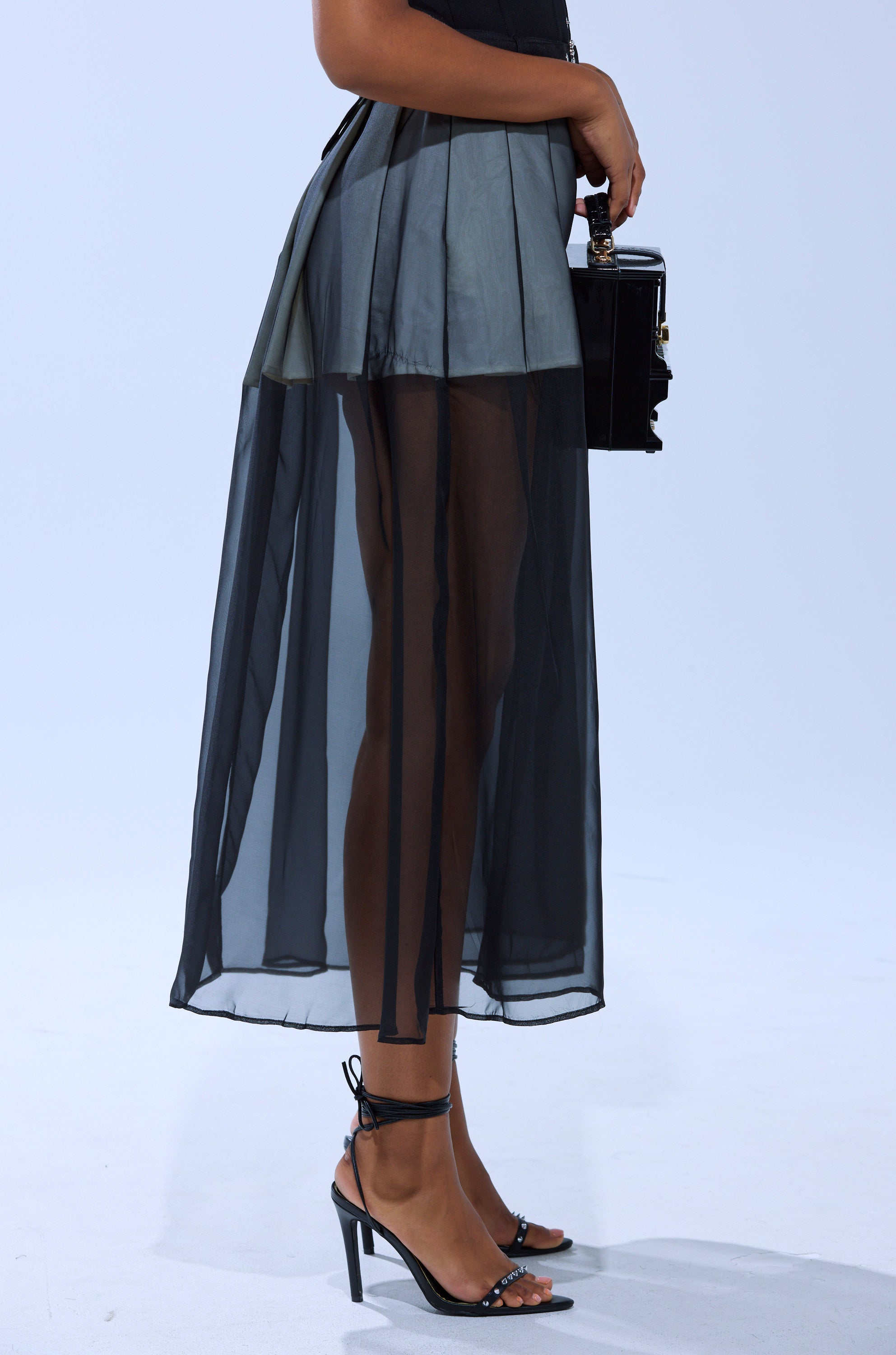 A person wearing the PARTY GIRL MIDI SKIRT paired with black strappy heels and a black handbag, standing against a plain light background.