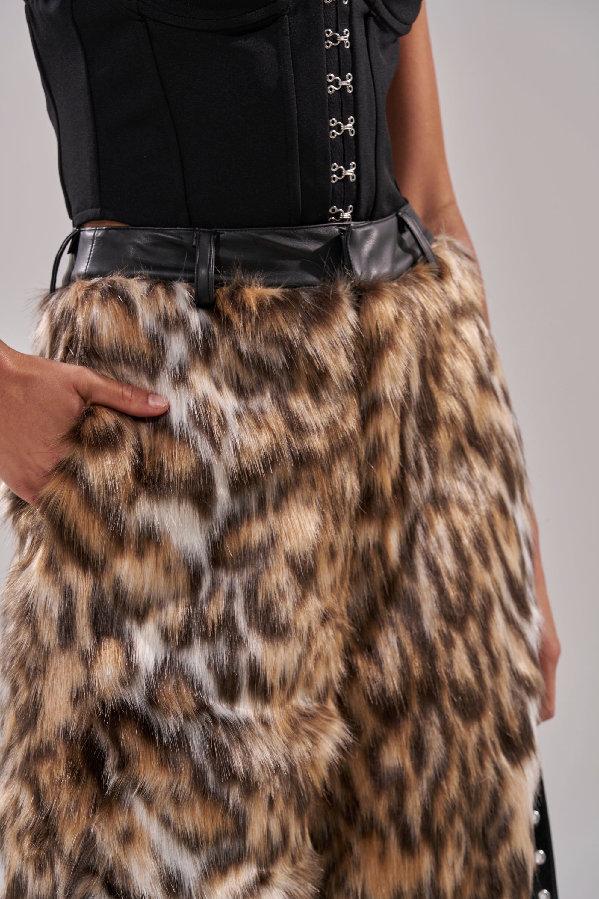 A person wears a black corset top with hook-and-eye closures and the CATCH ME IF YOU CAN LEOPARD FUR TROUSER, styled high-rise and wide-leg with a black belt. One hand is on their hip.