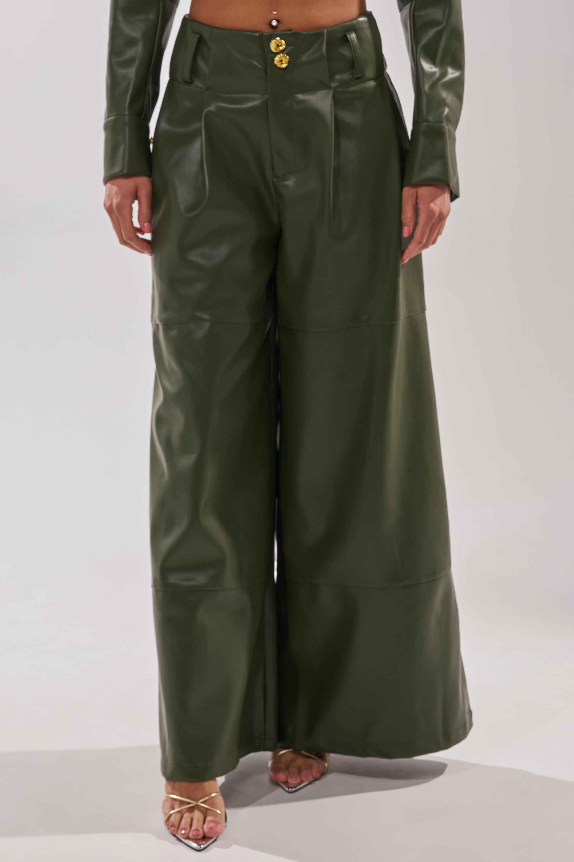 Wearing the REMEMBER YOU WIDE LEG TROUSER and an olive green jacket with gold sandals, this photo showcases the high-rise faux leather trousers and chic style from the shoulders down. 2