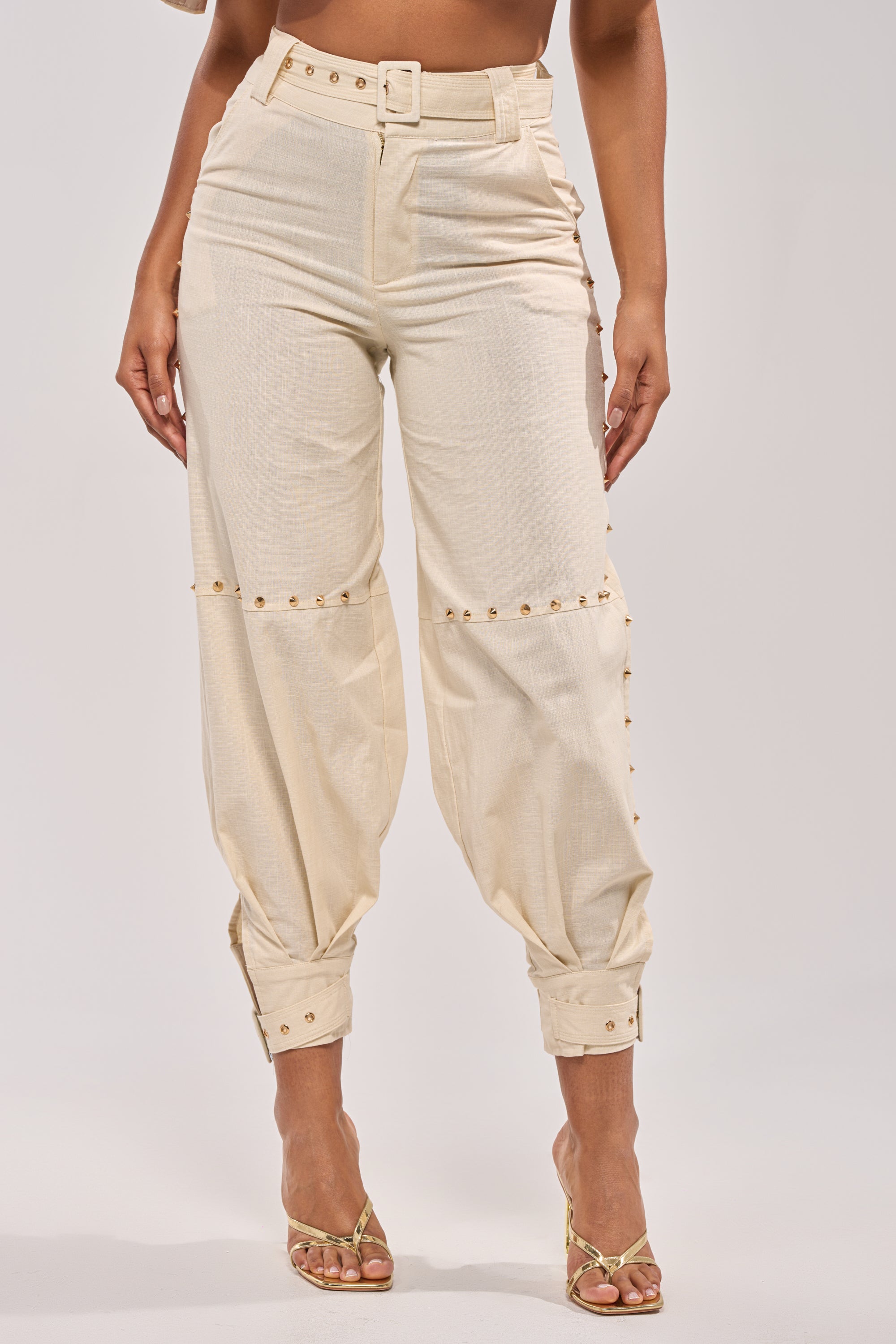 MAEVE LINEN STUDDED PANT styled with gold strappy heels, features high-rise waist and gold stud details along the seams and cuffs; model shown from waist to feet against a plain background. 1