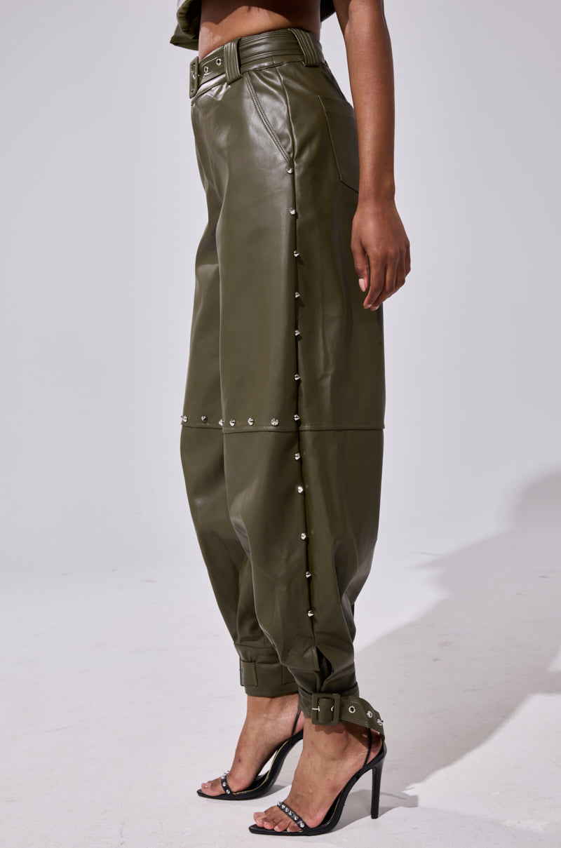 Wearing the STUDDED FAUX LEATHER BELTED PANT with silver snap buttons at the sides and ankles, paired with black high-heeled sandals, a person stands against a plain light background.