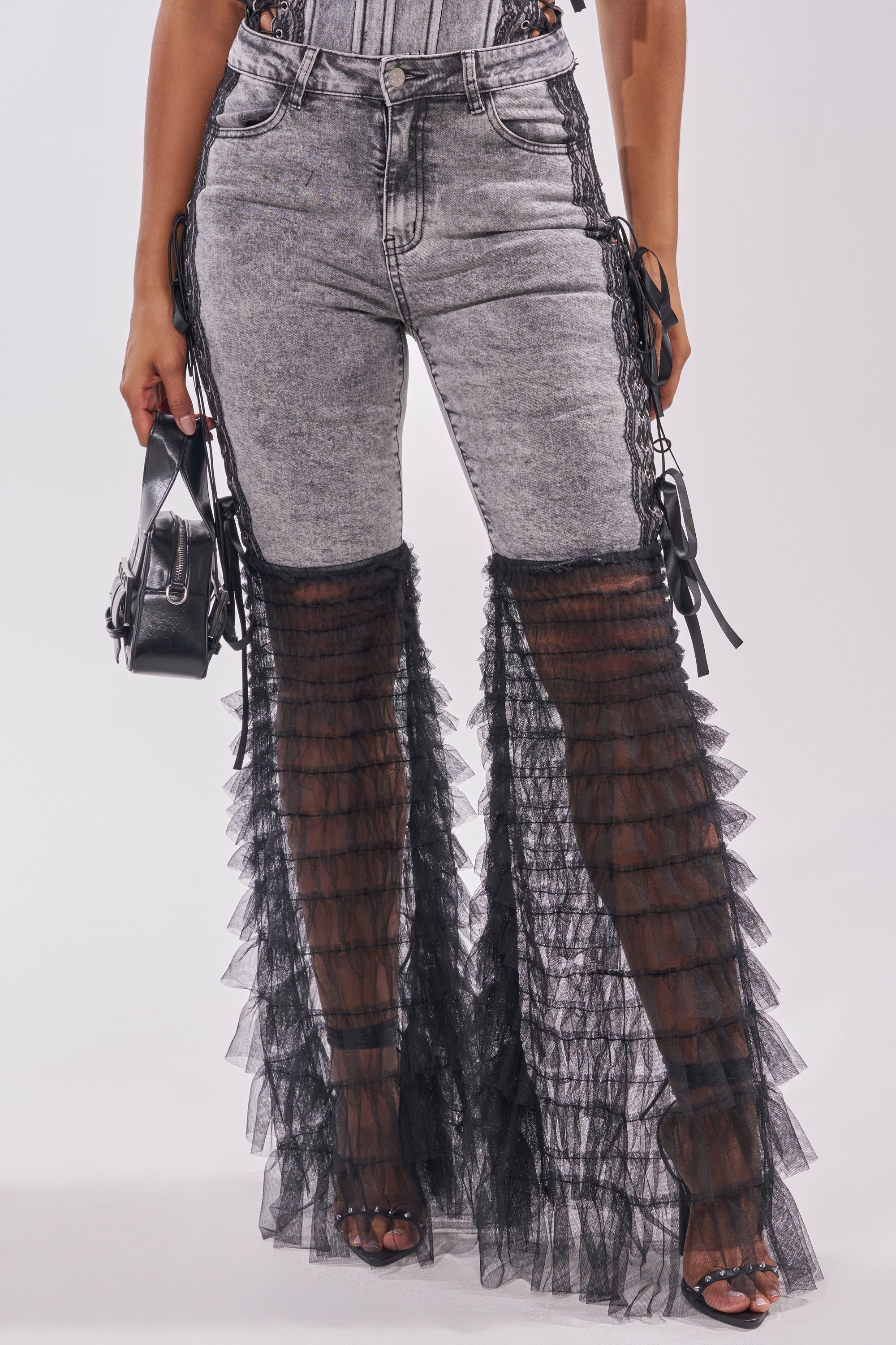 Wearing TICKED AND TIED LACE DETAIL FLARE DENIM—high-waisted, acid-wash flared jeans with black sheer ruffled tulle from the knees—paired with a small black handbag and black open-toe heels. Top not visible. 1