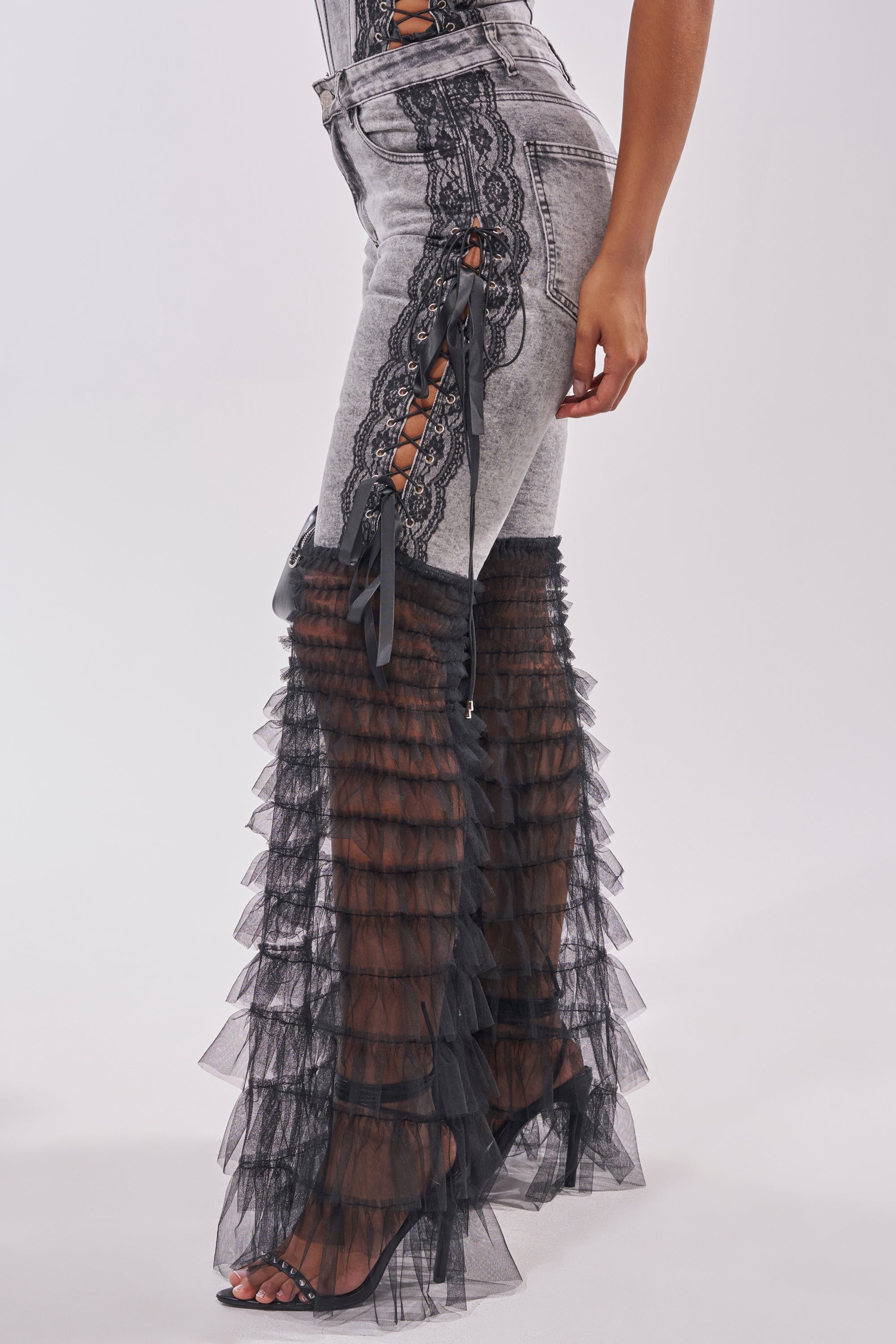 Wearing the TICKED AND TIED LACE DETAIL FLARE DENIM—flared jeans with black lace-up sides and sheer, ruffled tulle from the knees down—paired with open-toed heels brings a bold twist to classic denim style. 3