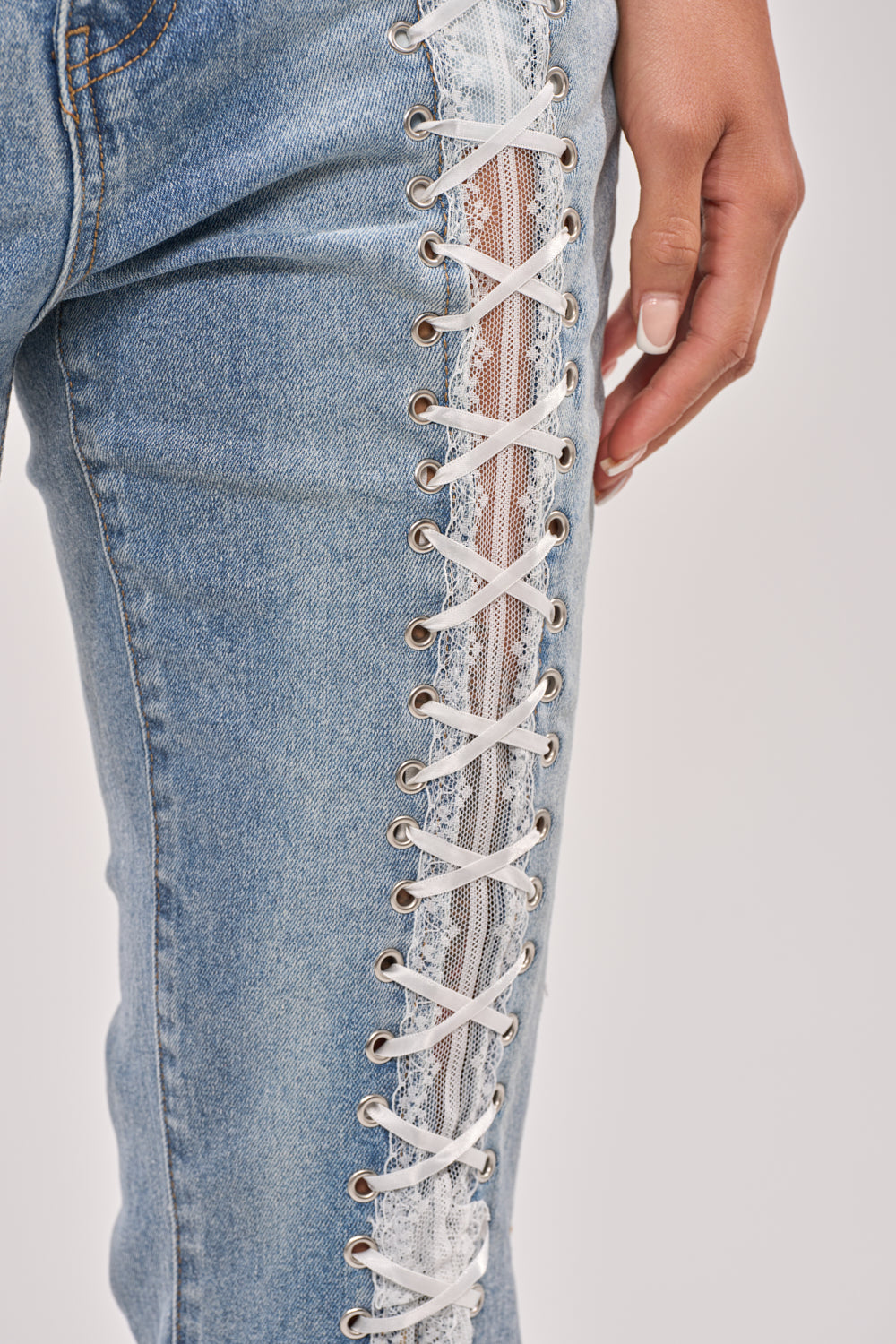 Close-up of a person wearing LOVE ME LIKE THAT LACE UP FLARE DENIM, featuring white lace-up detail and sheer lace insert along the outer seam. Their hand rests near the hip, highlighting manicured nails—a coquette statement. 10