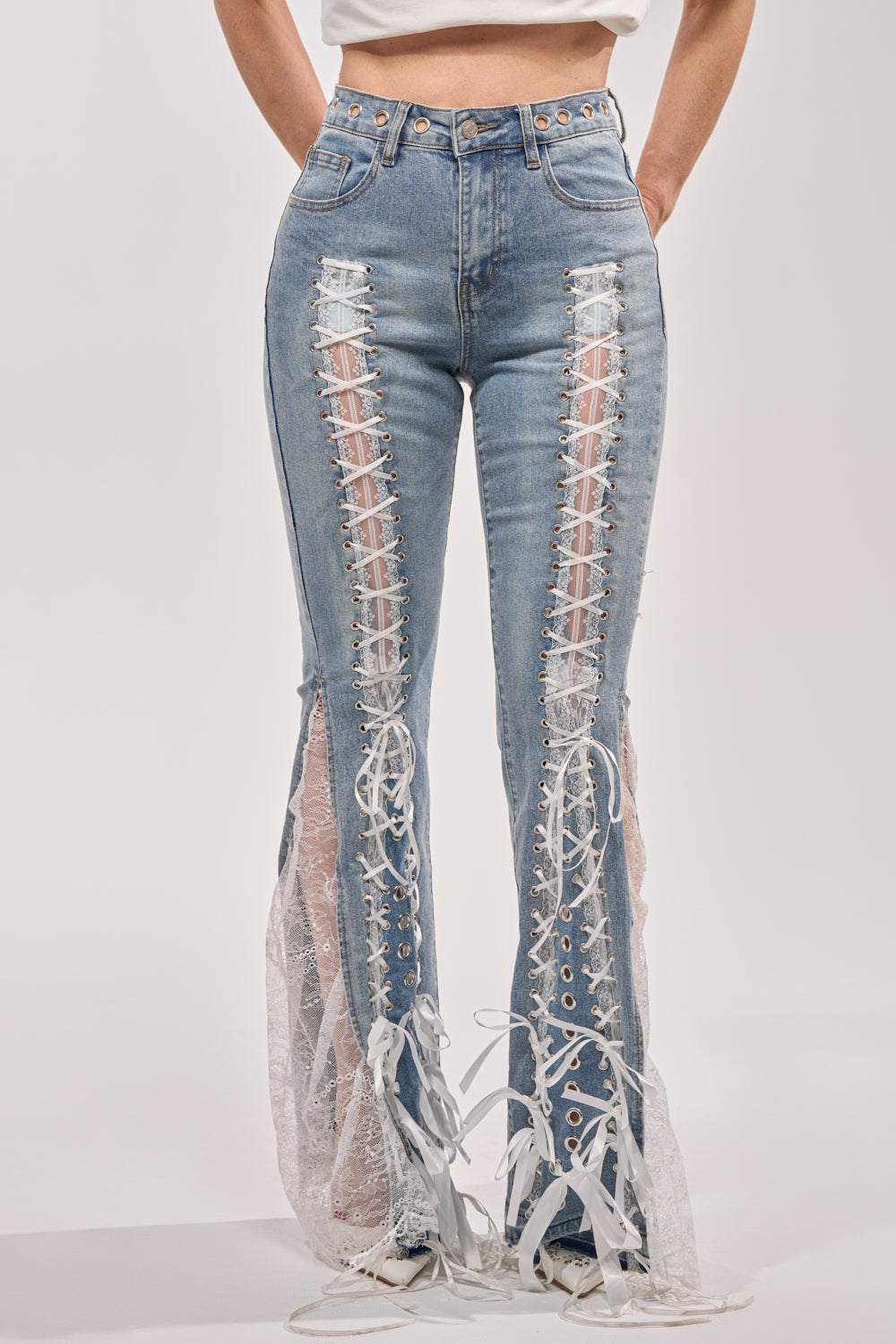 A person wears the LOVE ME LIKE THAT LACE UP FLARE DENIM: high-rise flared jeans featuring sheer lace and white lace-up panels along the front and sides. Only their lower torso and legs are visible. 3