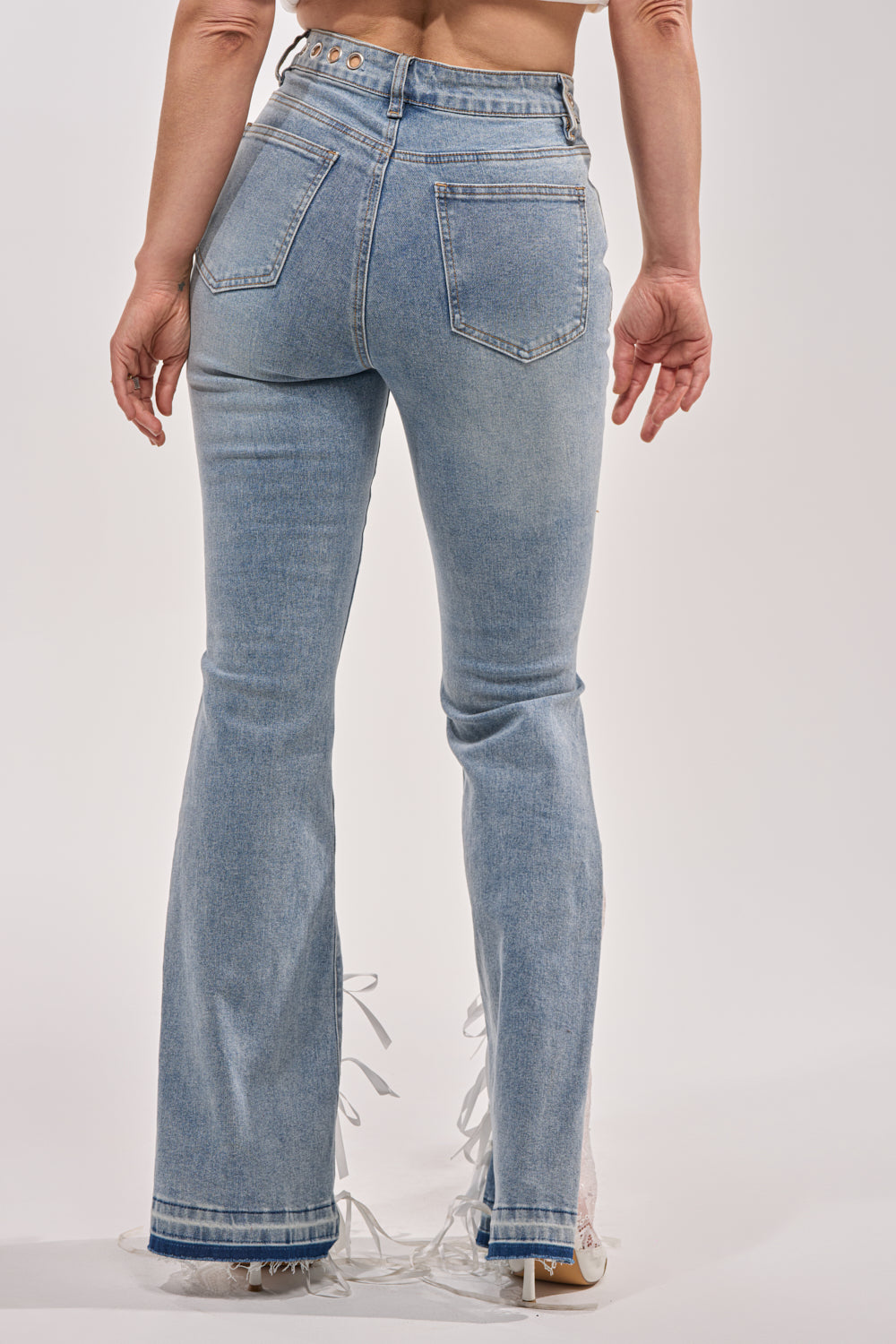 Someone is seen from the back wearing LOVE ME LIKE THAT LACE UP FLARE DENIM—light blue, high-rise, fitted through the legs with flared frayed hems and two back pockets. The background is plain white. 5