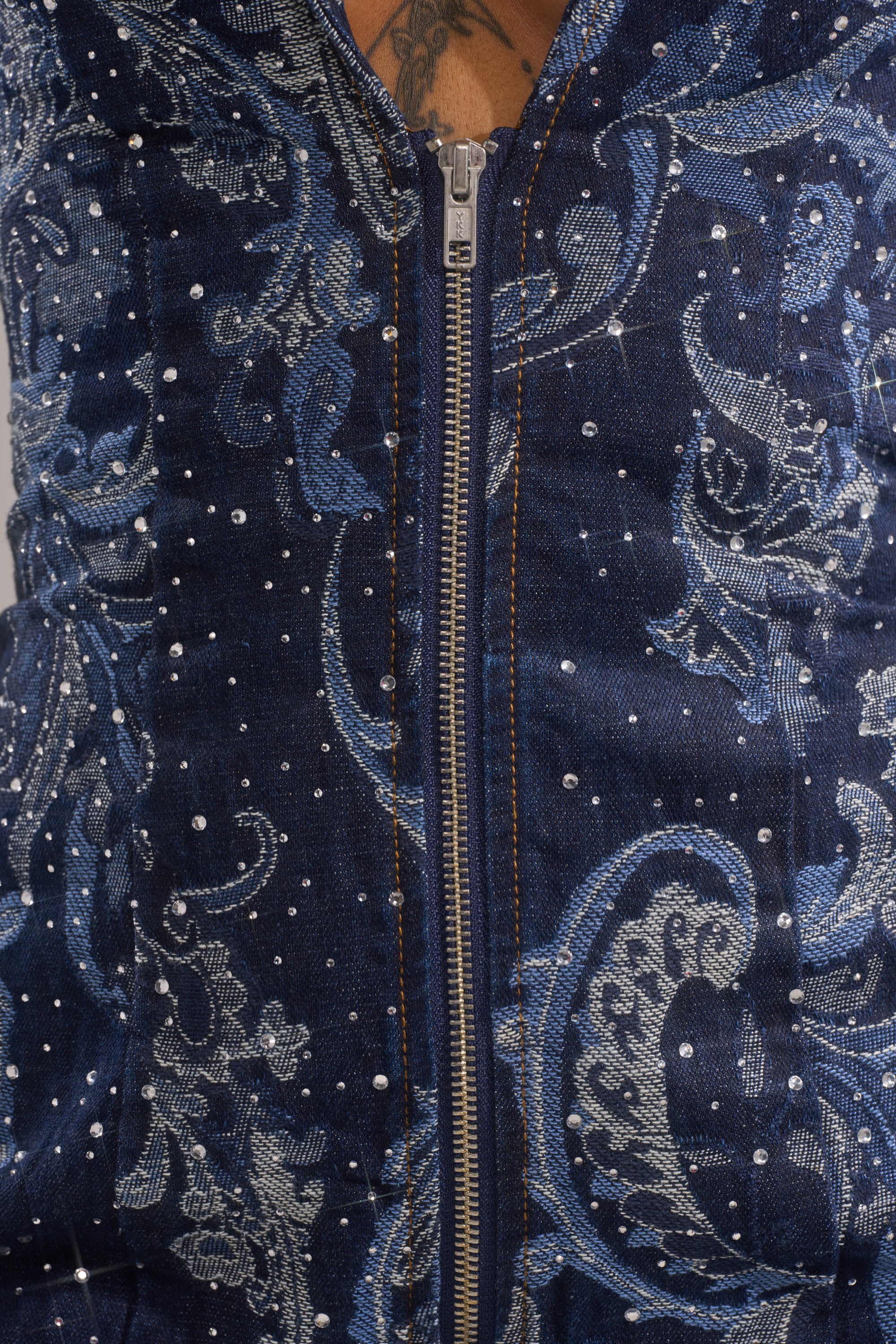 Close-up of the INTO SOMETHING BETTER DENIM BLAZER MINI DRESS: blue denim with a silver zipper, intricate light blue floral patterns, white beads and dots, sparkling rhinestones, and a tattoo visible above the zipper.