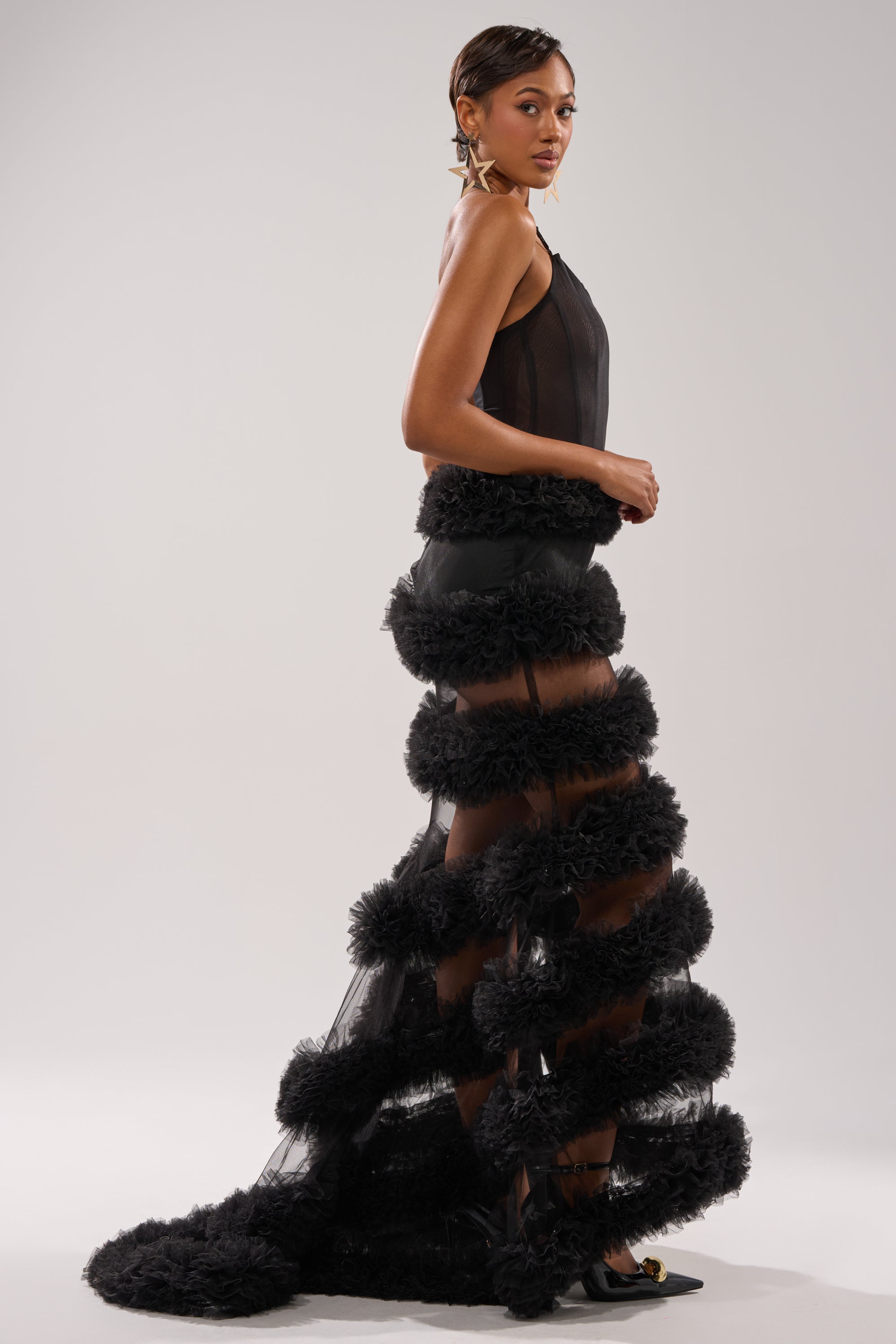 A woman models the QUEEN OF EVERYTHING MAXI DRESS, featuring a sheer black top and dramatic layered tulle skirt with a corset-style bodice, creating a bold, structured look against a plain light background. 2