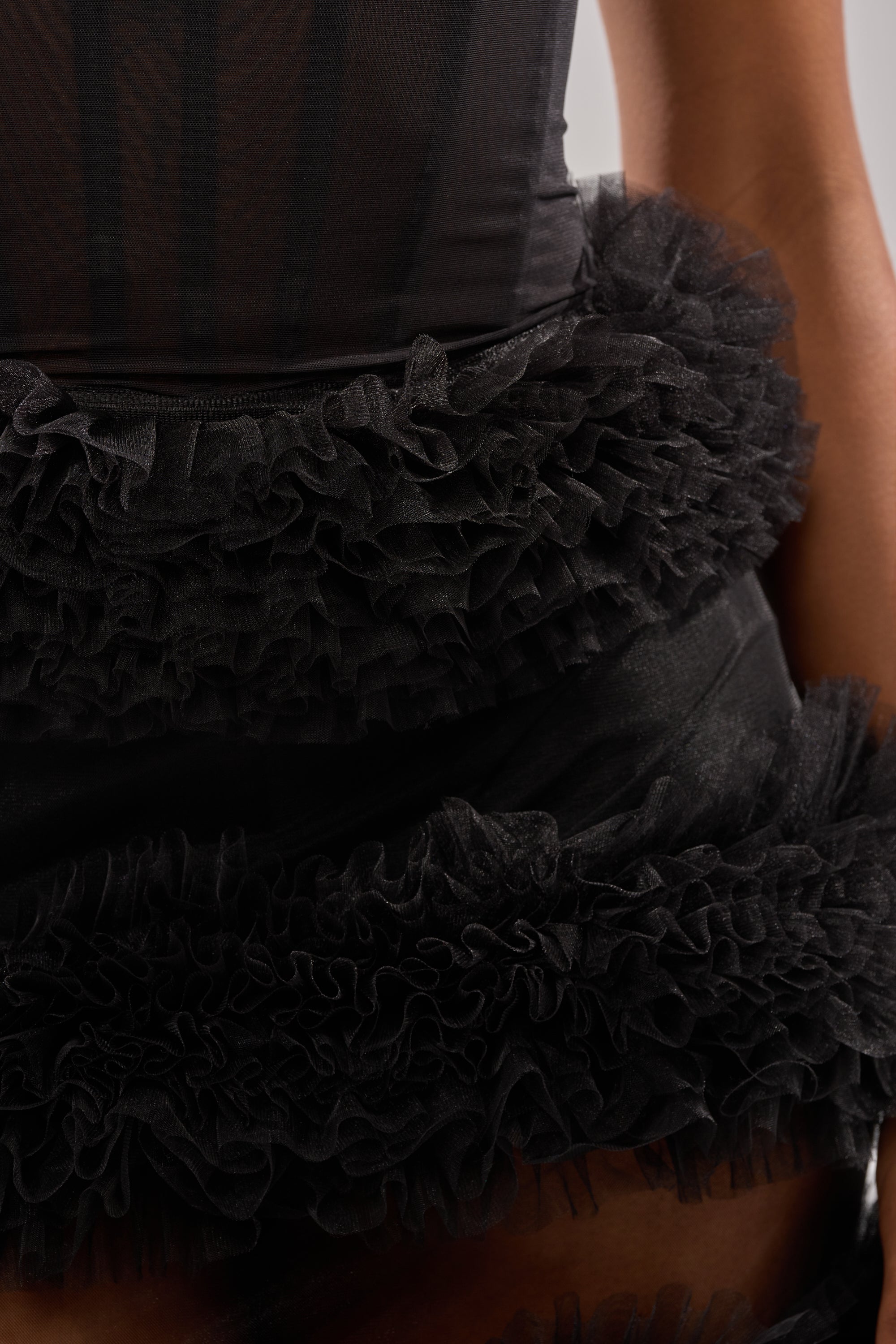 Close-up of a person wearing the QUEEN OF EVERYTHING MAXI DRESS, showcasing its black sheer tulle top and skirt with layered ruffled tulle at the waist and hip, emphasizing textured detailing. 4