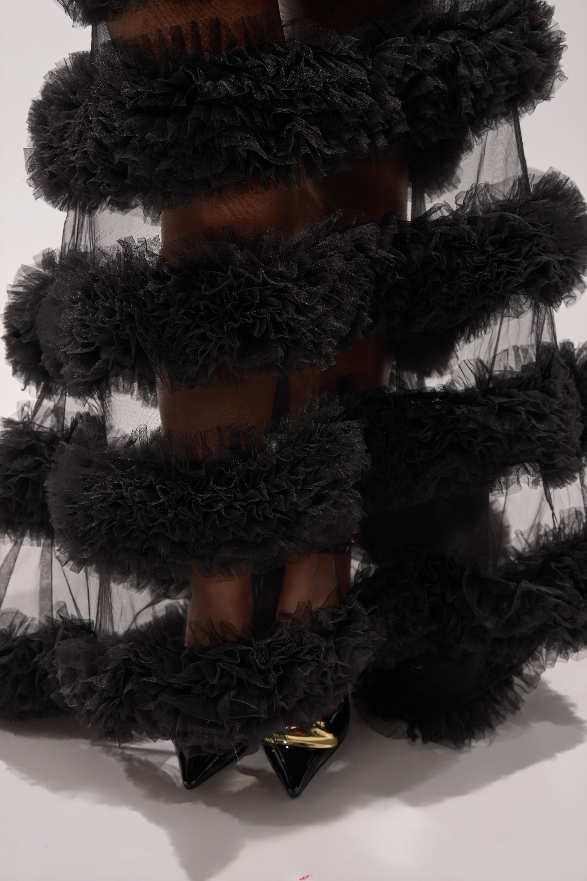 Close-up of the QUEEN OF EVERYTHING MAXI DRESS, showcasing sheer tulle and layered ruffles. The corset-style bodice completes the look, paired with black pointed-toe heels with a gold accent visible beneath. 5