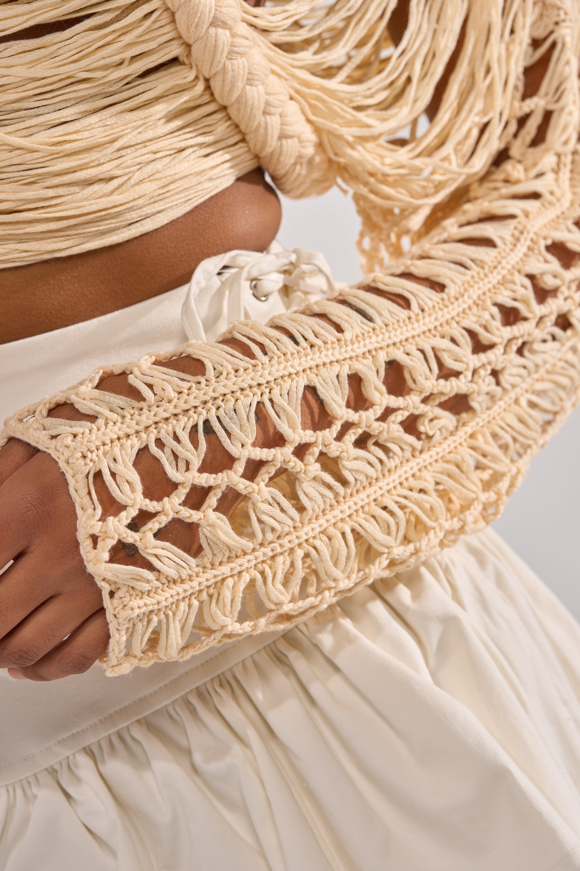 Close-up of a person wearing the CATCHING FEELING FRINGE SWEATER in cream, featuring intricate knit details over a white gathered skirt. The texture of the yarn and fabric stands out vividly. 6