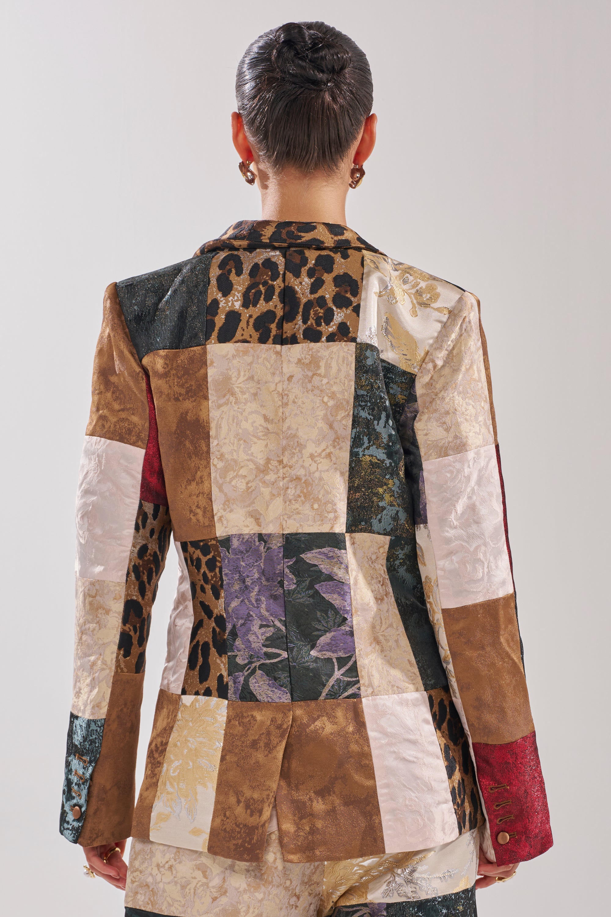 A person with short, slicked-back hair is shown from behind wearing the MADE YOU LOOK PATCHWORK BLAZER, a mixed-media jacket featuring florals, animal prints, and solid color panels.