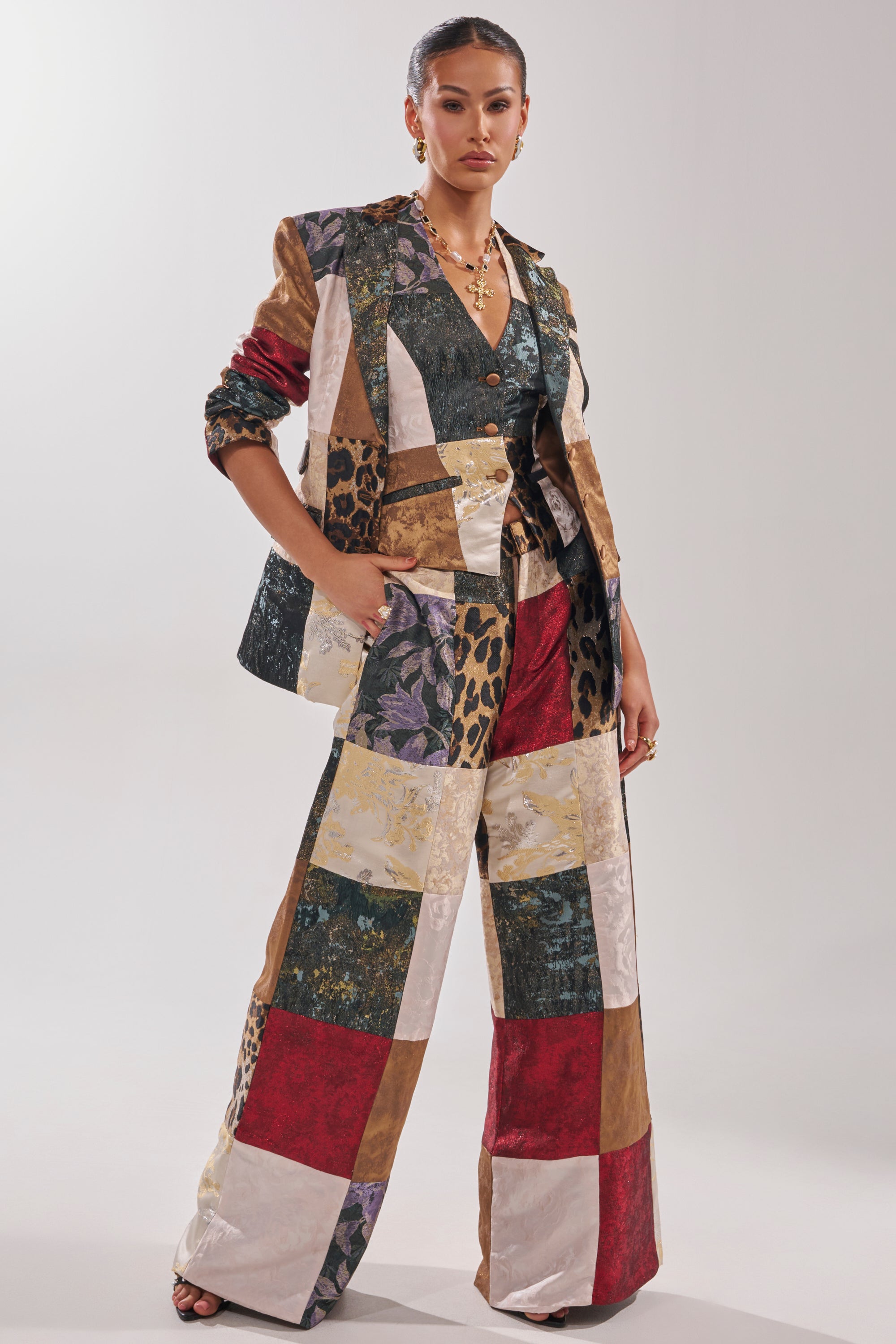 A woman poses confidently with her hand in her pocket, wearing the MADE YOU LOOK PATCHWORK BLAZER—an eye-catching mix of animal print, florals, and solids—styled with wide-leg pants and bold jewelry.