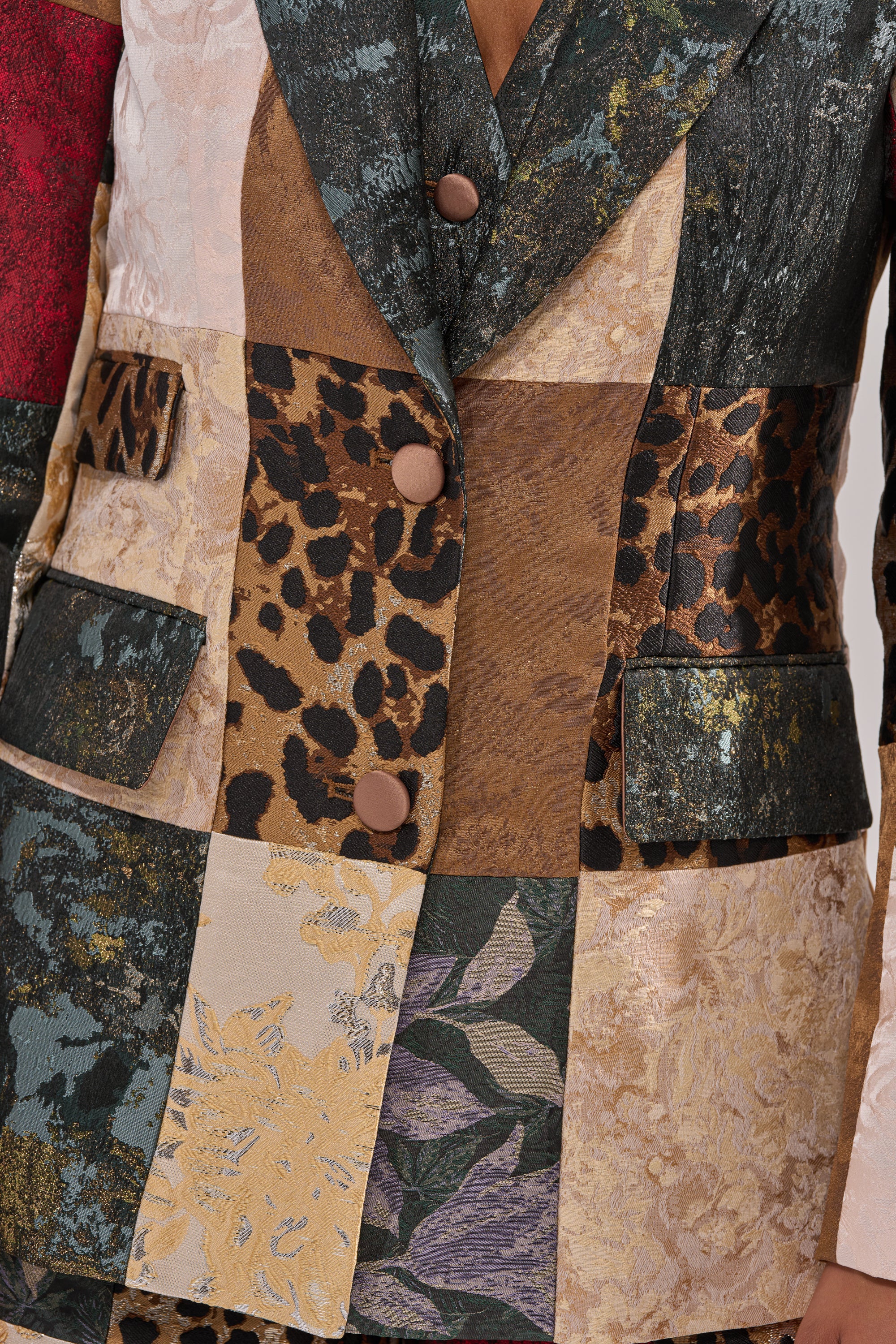 The MADE YOU LOOK PATCHWORK BLAZER showcases a tailored design with flap pockets, three brown buttons, and textured fabric squares including leopard print, metallics, florals, and brocade patterns in earth tones.