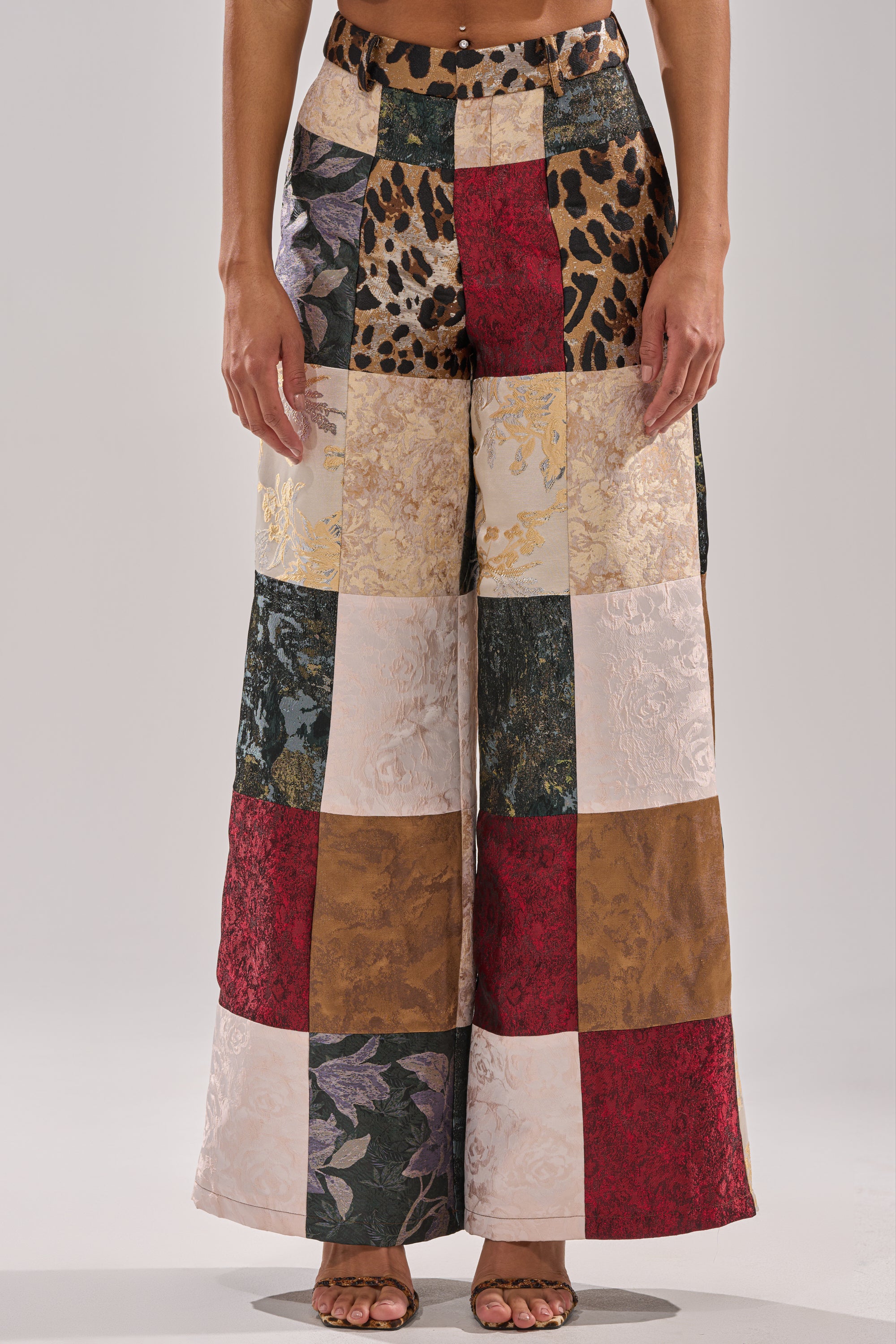 A person stands against a plain light background wearing the MADE YOU LOOK PATCHWORK TROUSER—high-rise, wide-leg pants crafted from colorful patchwork fabrics with floral, animal, and brocade patterns.