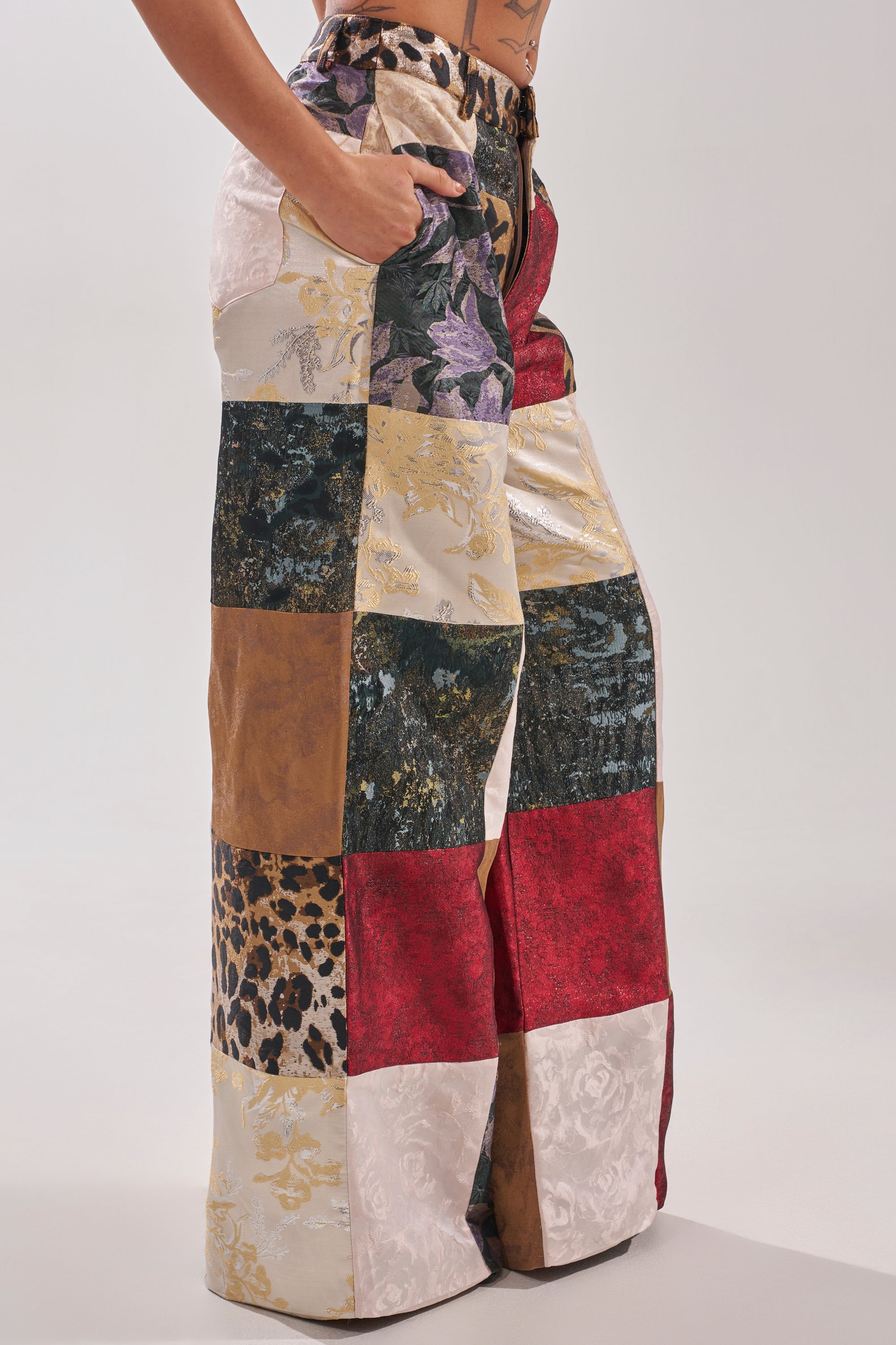 A person stands with hands in pockets, highlighting the MADE YOU LOOK PATCHWORK TROUSER—high-rise and wide-leg, crafted from eclectic fabrics including animal prints, metallics, florals, and rich solids.