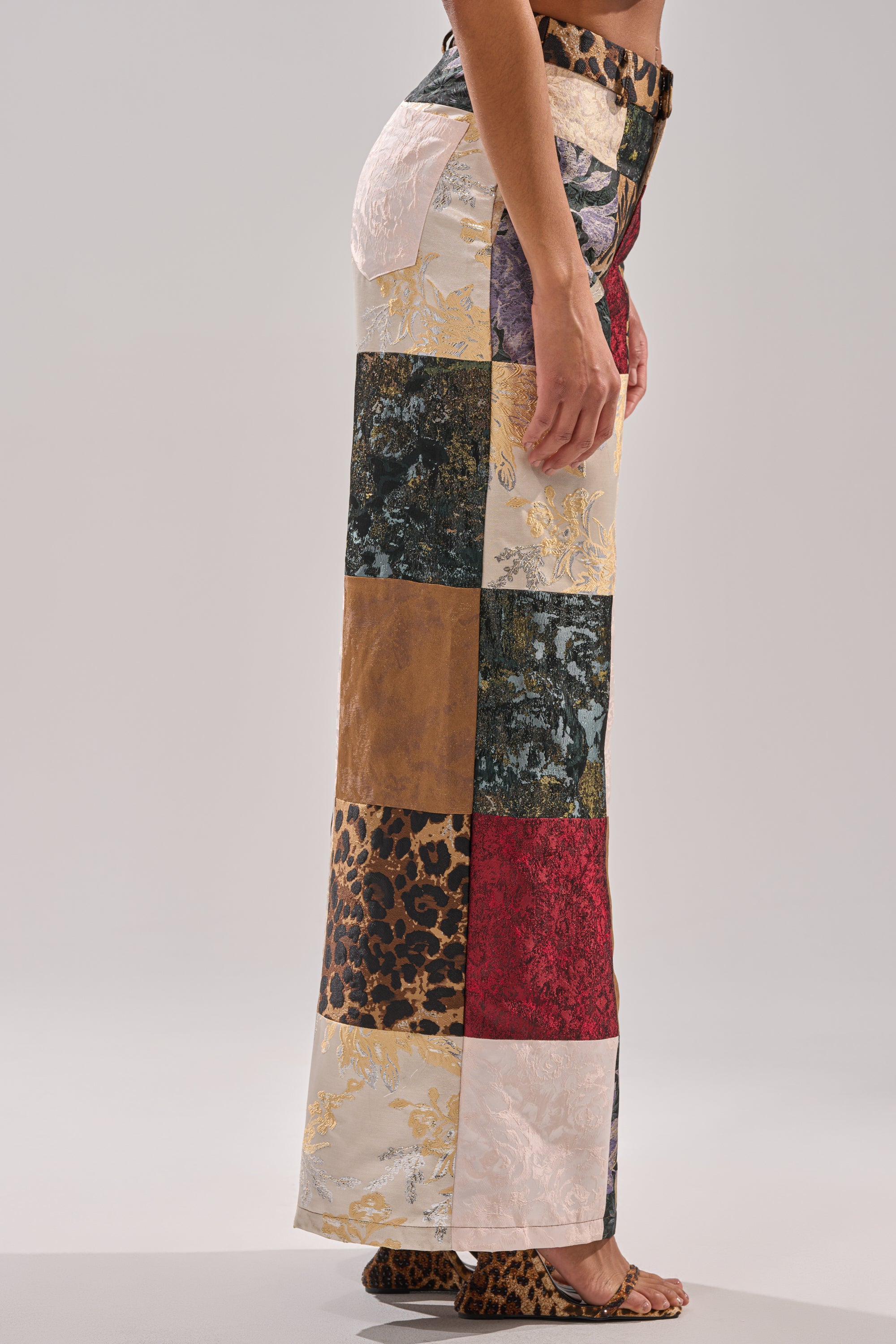 A person wears the MADE YOU LOOK PATCHWORK TROUSER—high-waisted with textured patchwork, including velvet and leopard print—styled with open-toe leopard print heels for a bold, dramatic look.
