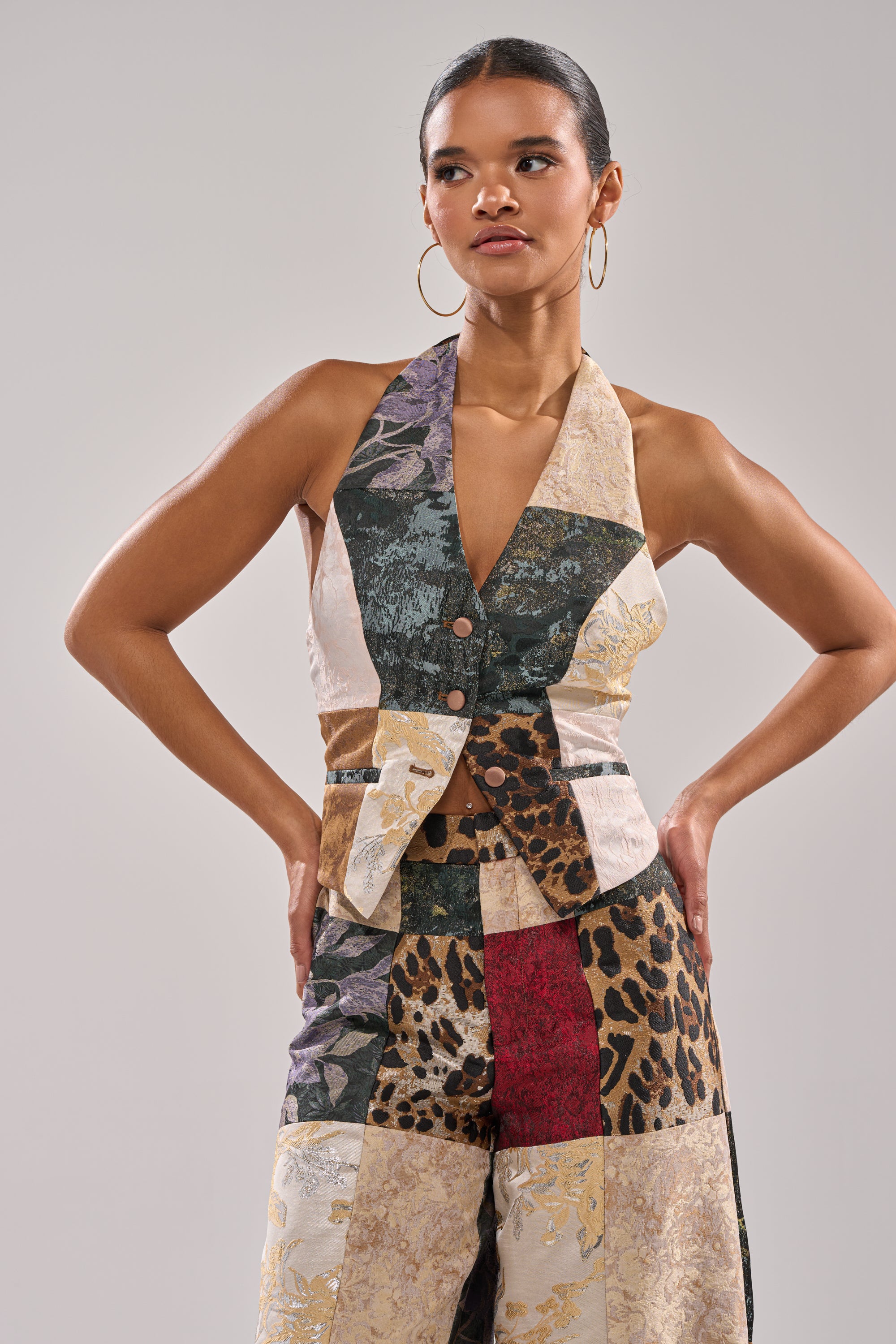 A woman stands with her hands on her hips, wearing the MADE YOU LOOK PATCHWORK HALTER VEST and high-waisted multicolored pants with animal print and floral patterns.