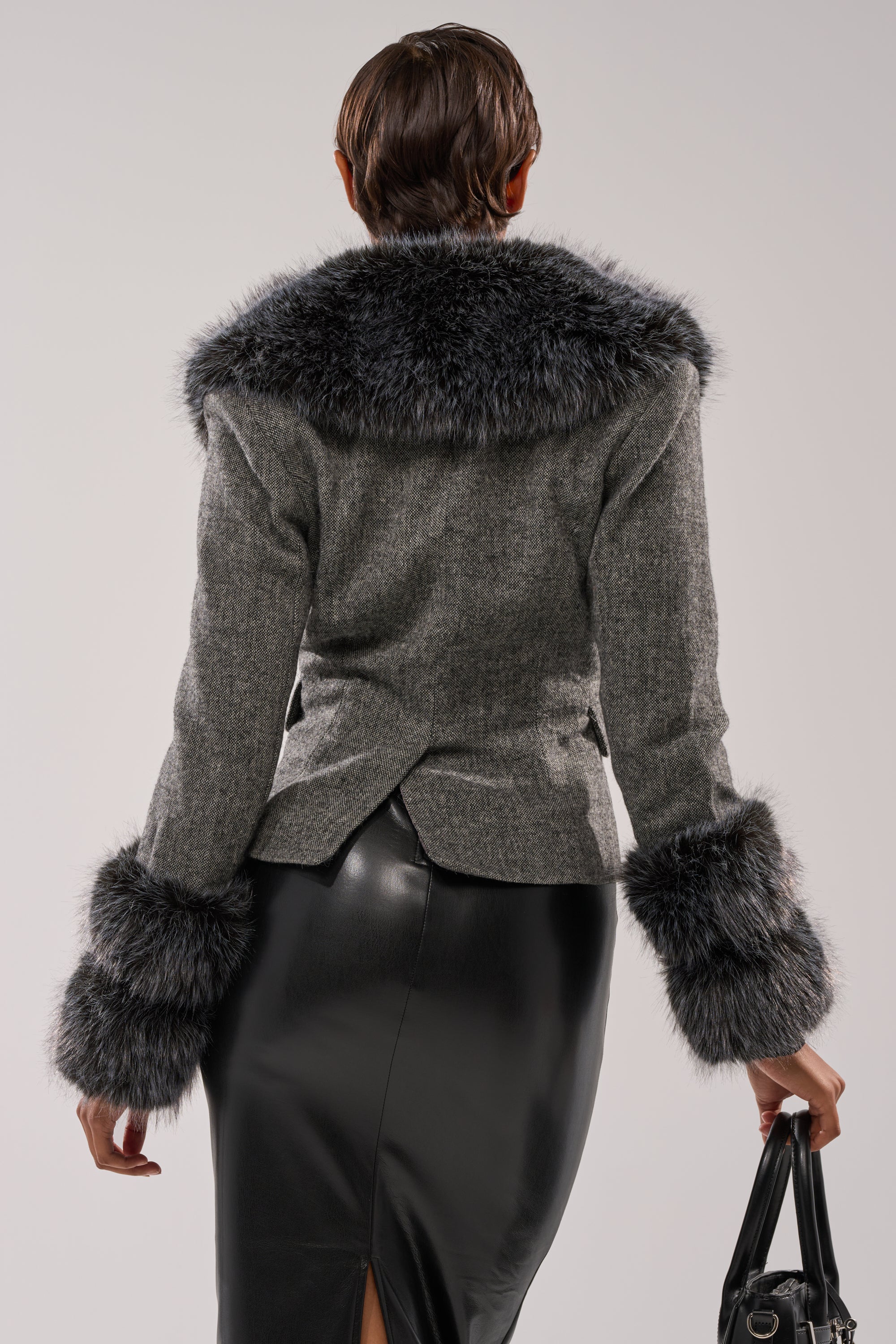 A person with short brown hair, seen from behind, is wearing the I SEE LONDON FUR TRIM BLAZER, a black leather skirt, and holding a black handbag.