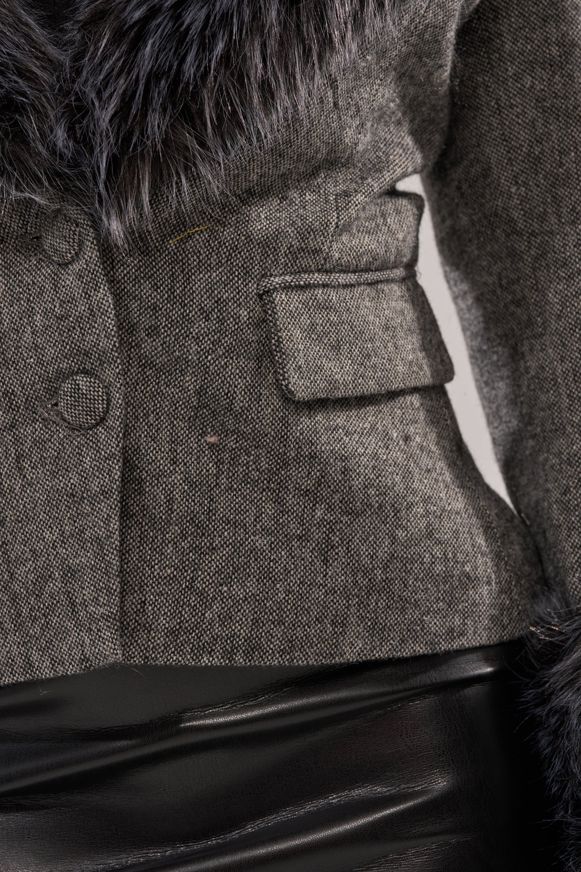 Close-up of a person wearing the I SEE LONDON FUR TRIM BLAZER, a gray wool-blend cropped blazer with faux fur trim, flap pocket, and button details, paired with a black leather skirt.