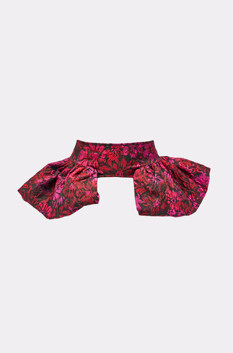 The NIGHTLY FLORAL PEPLUM BELT is a cropped, structured jacquard top with a wide waistband and dramatic puffed sleeves, featuring pink and red floral patterns on a dark background, shown against a white backdrop.