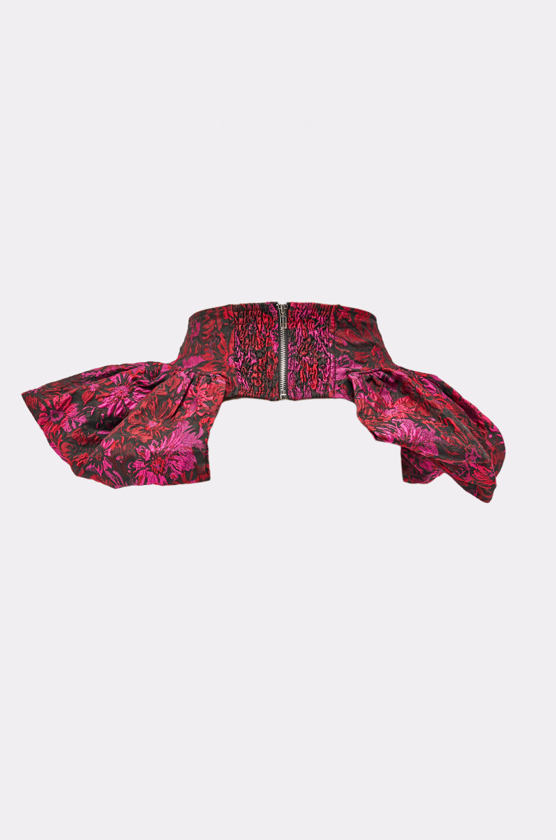 The NIGHTLY FLORAL PEPLUM BELT is a stylish pink and red jacquard accessory with a front zipper and bold ruffled sides, offering gothic-chic flair—shown on a plain white background.