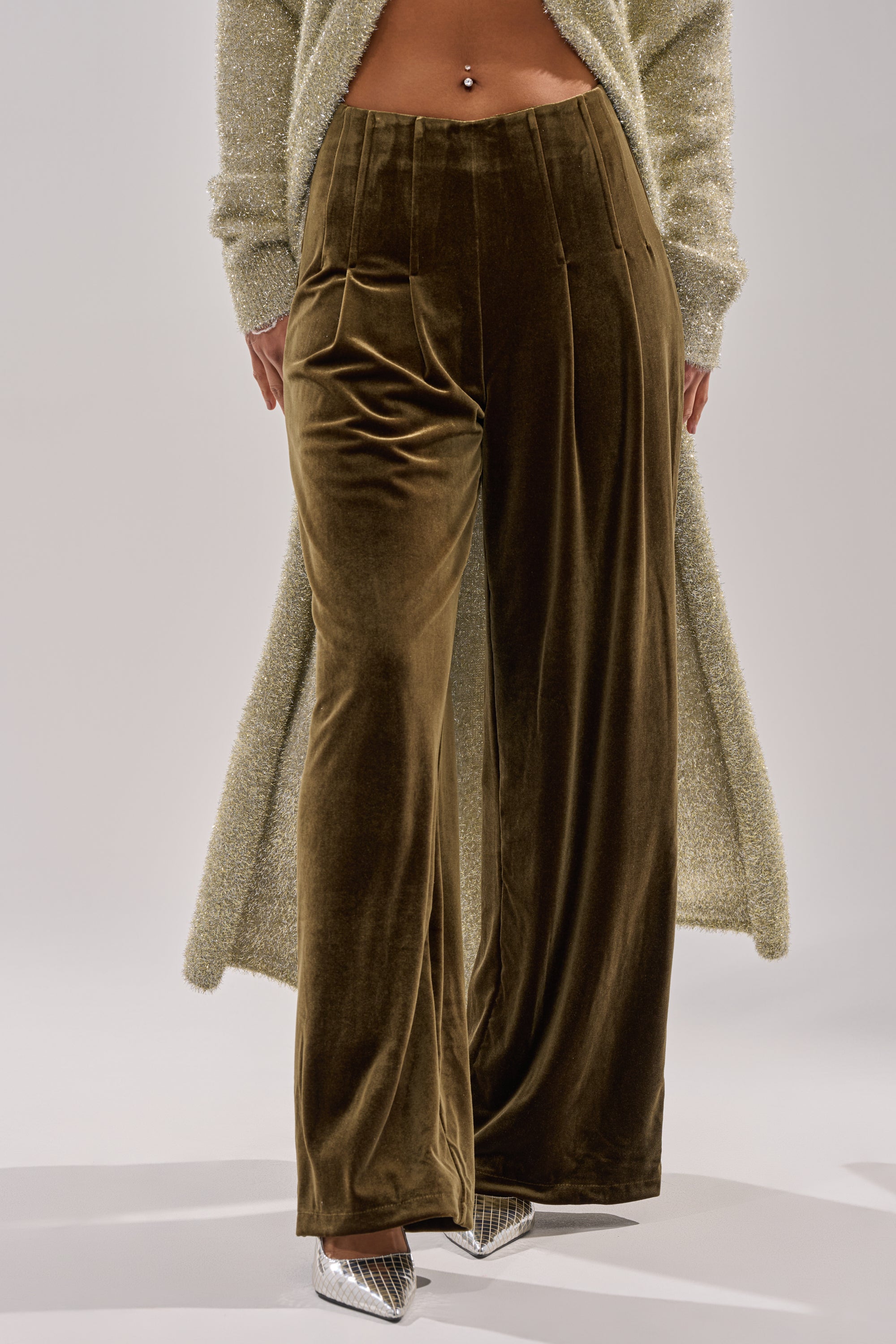 Wearing the SHOW ME IT TROUSER in high-rise, wide-leg brown velvet, paired with a sparkly long cardigan and silver pointed-toe heels. A midriff-baring look and navel piercing complete this bold, chic ensemble.