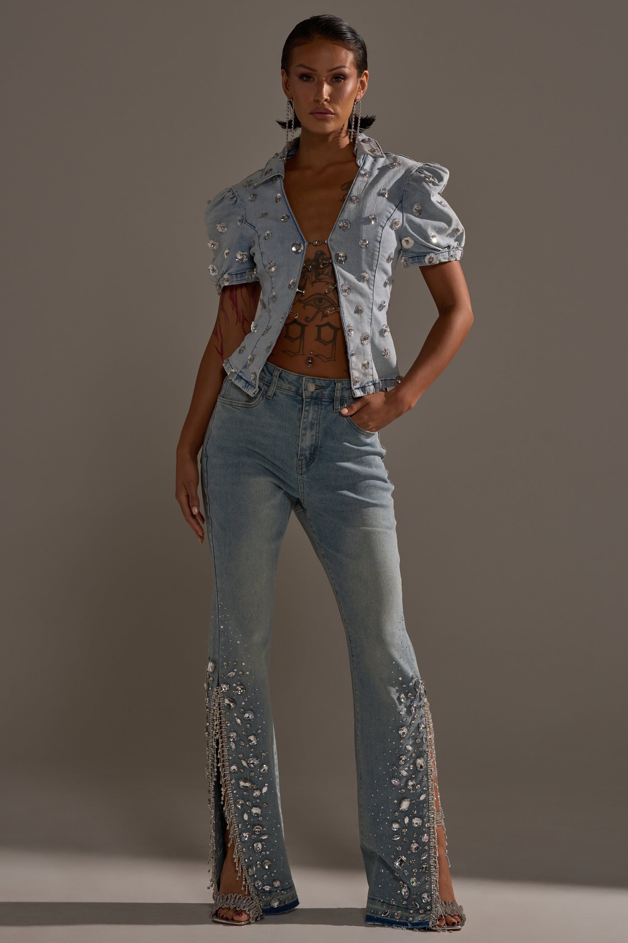 A woman stands against a plain background wearing the STAR GIRL RHINESTONE DENIM set: a light blue jacket with puffed sleeves, pearl and rhinestone accents, and matching high-rise jeans featuring pearls and side slits.