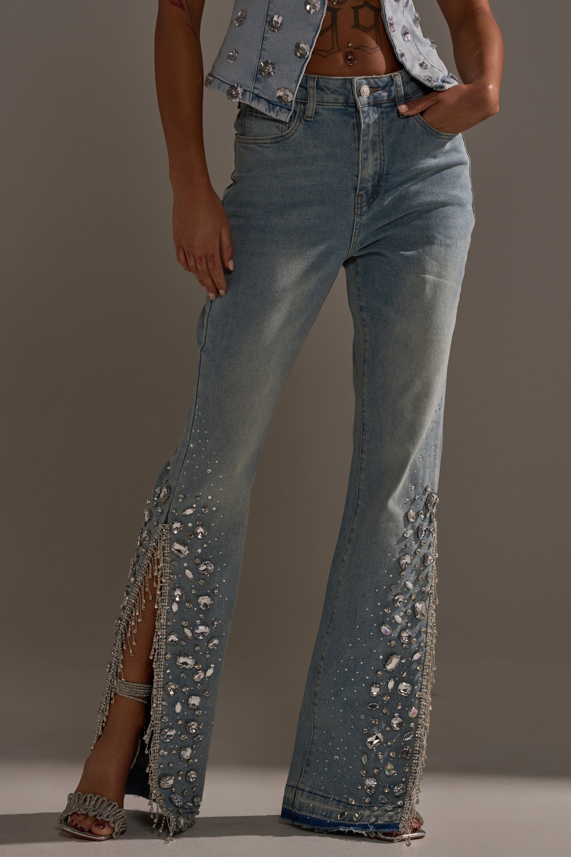A person wearing the STAR GIRL RHINESTONE DENIM: light blue, high-rise jeans with rhinestone and crystal embellishments, fringe on flared legs, paired with a matching denim vest.