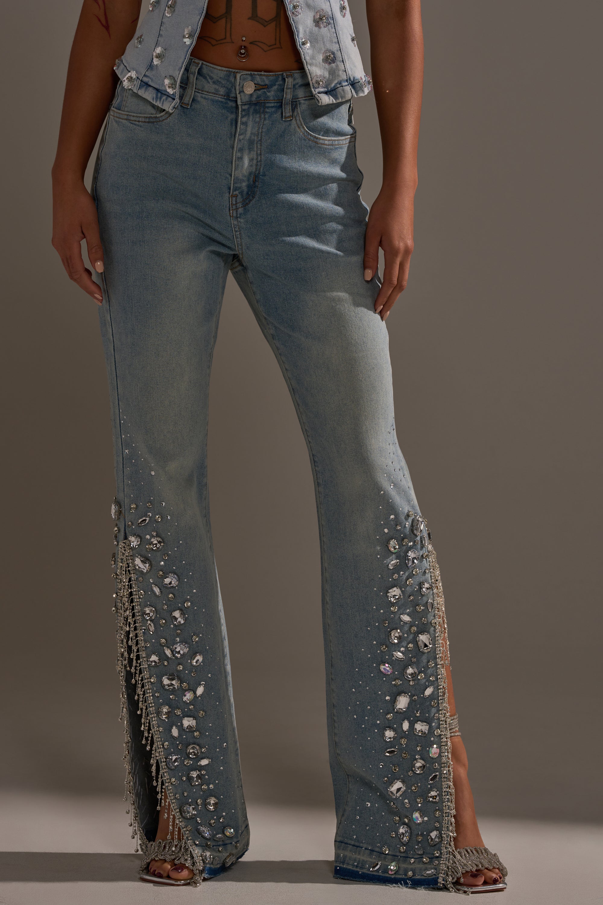 Wearing the STAR GIRL RHINESTONE DENIM jeans with pearls, rhinestones, and fringe-trimmed side slits, styled perfectly with a matching denim vest.