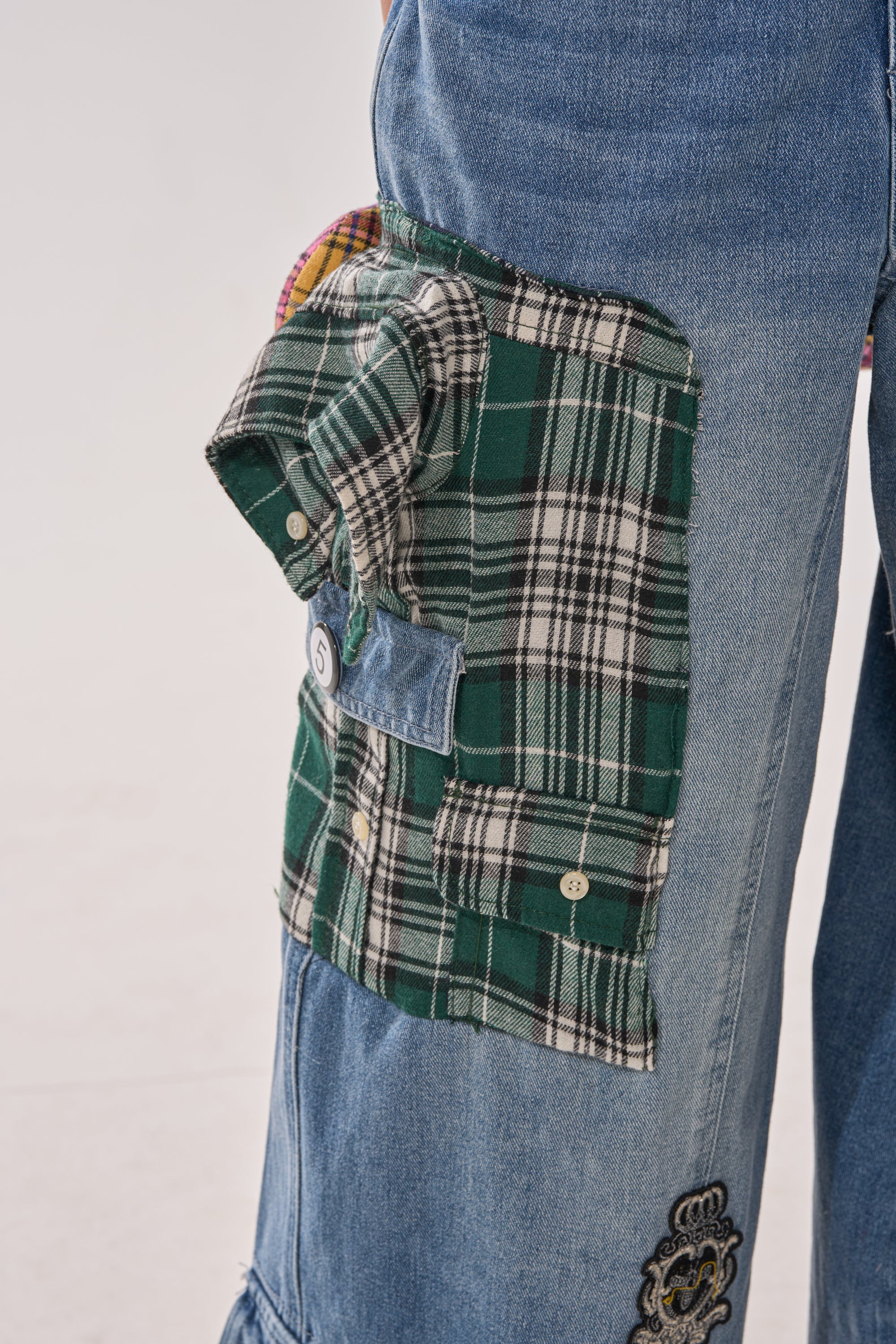 A close-up of FEELING THE WAVES RELAXED DENIM, wide-leg pants featuring a large green plaid cargo-style side pocket with button accents and contrasting textures. 7