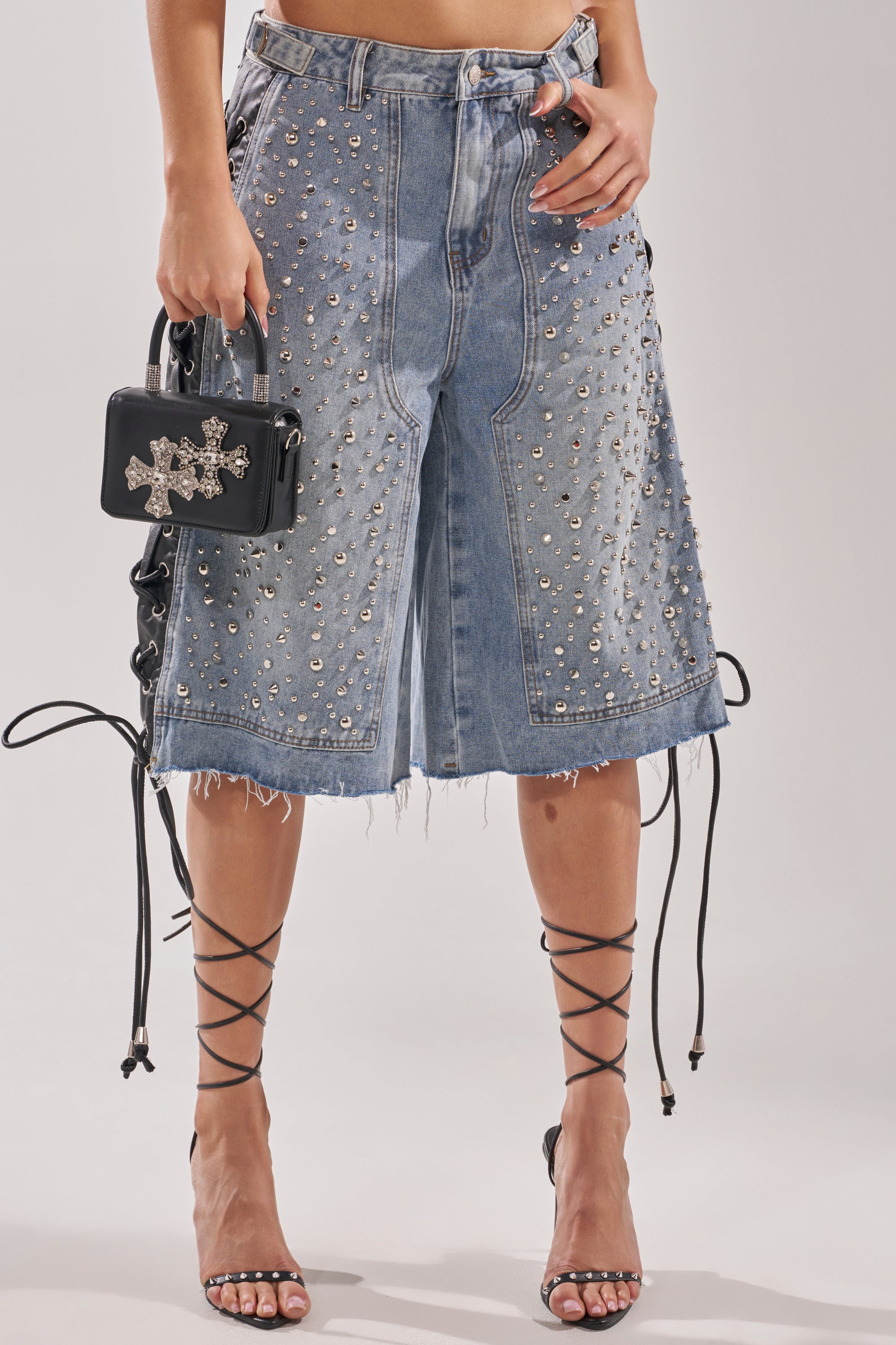 Wearing HONEY BABY BERMUDA SHORTS, strappy black high heels, and holding a small black handbag with star-shaped embellishments; only the lower half of the body is shown. 3