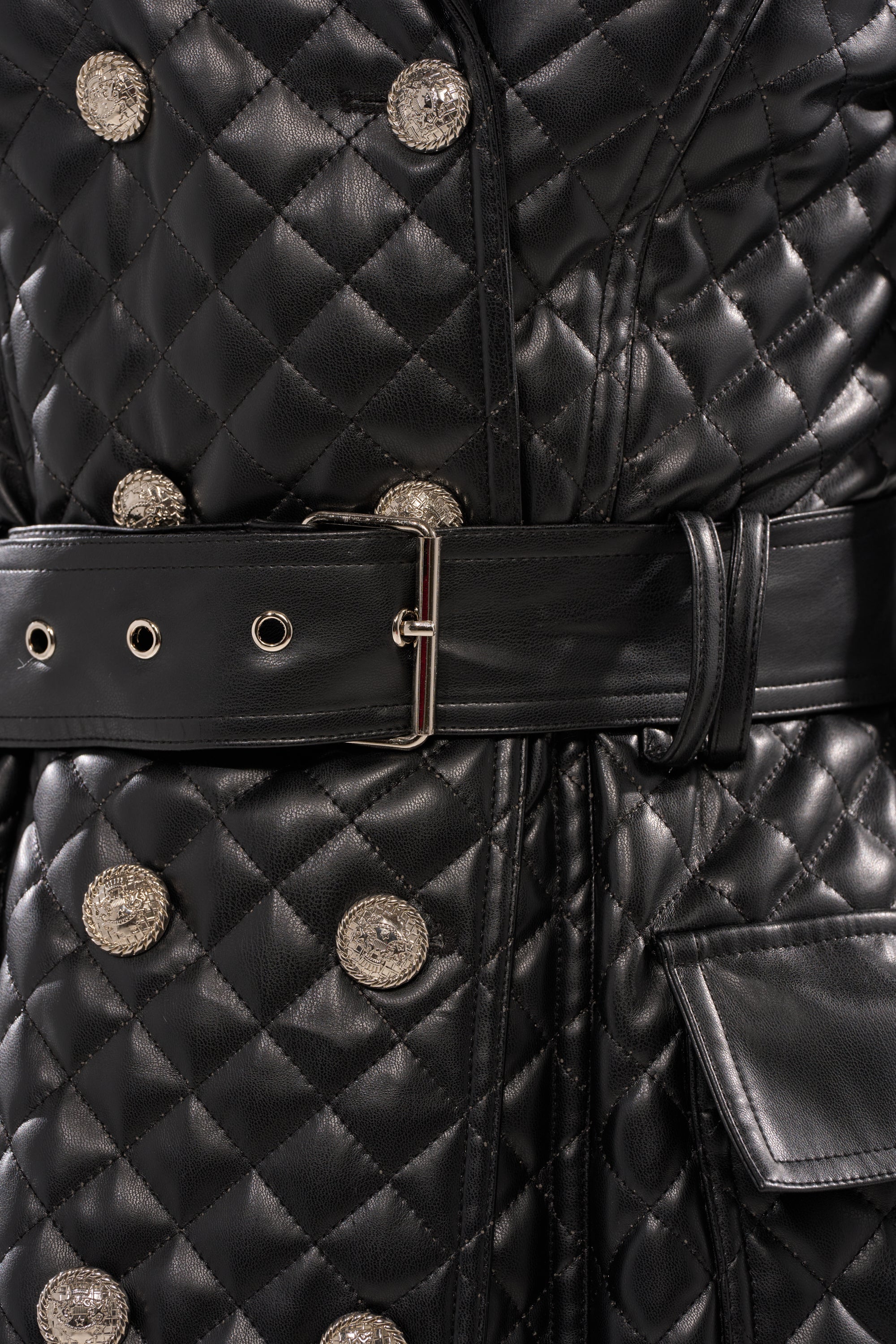 Close-up of the MADISON AVE QUILTED TRENCH: a black quilted coat with metallic buttons, a wide black leather belt with a rectangular silver buckle, and a flap pocket.