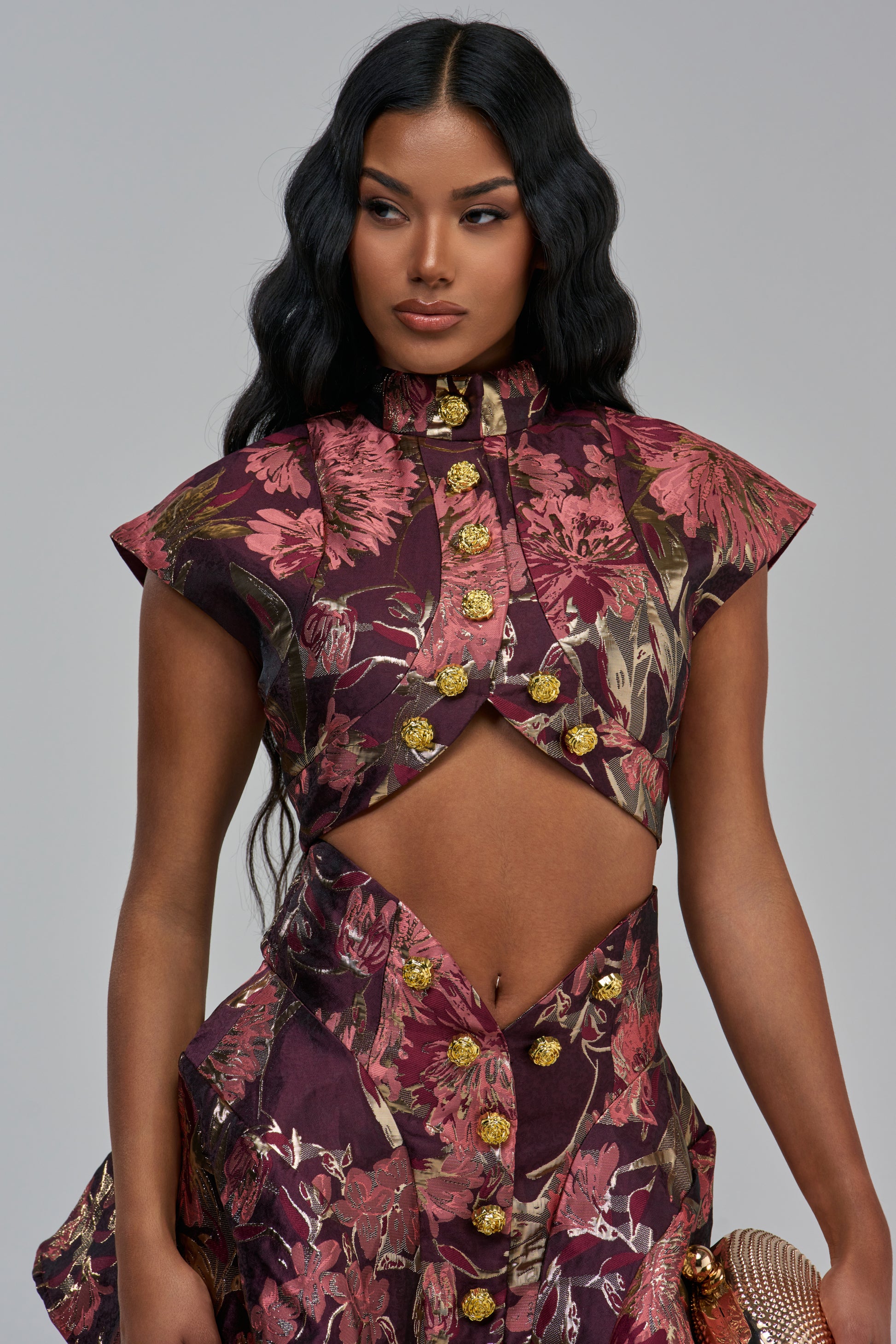 KAYLA BROCADE SLEEVELESS BLOUSE IN PURPLE MULTI: a purple and pink floral brocade sleeveless top with a cropped silhouette, featuring gold buttons and a front cutout.