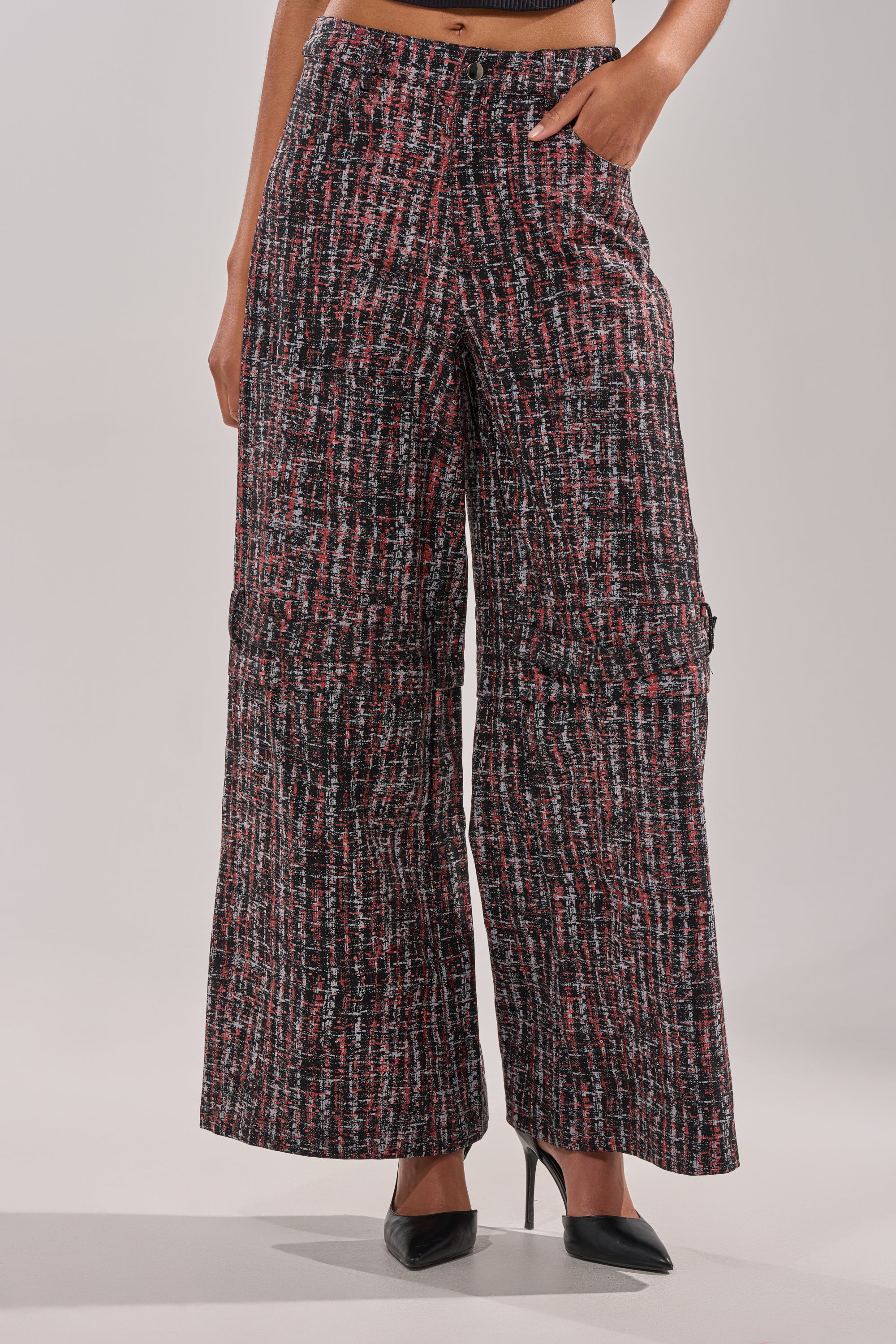 A person wears the WORK IT FAUX LEATHER PLAID TROUSER—high-rise, wide-leg plaid cargo trousers in red, black, and white—with one hand in the pocket, styled with black pointed-toe heels. 1