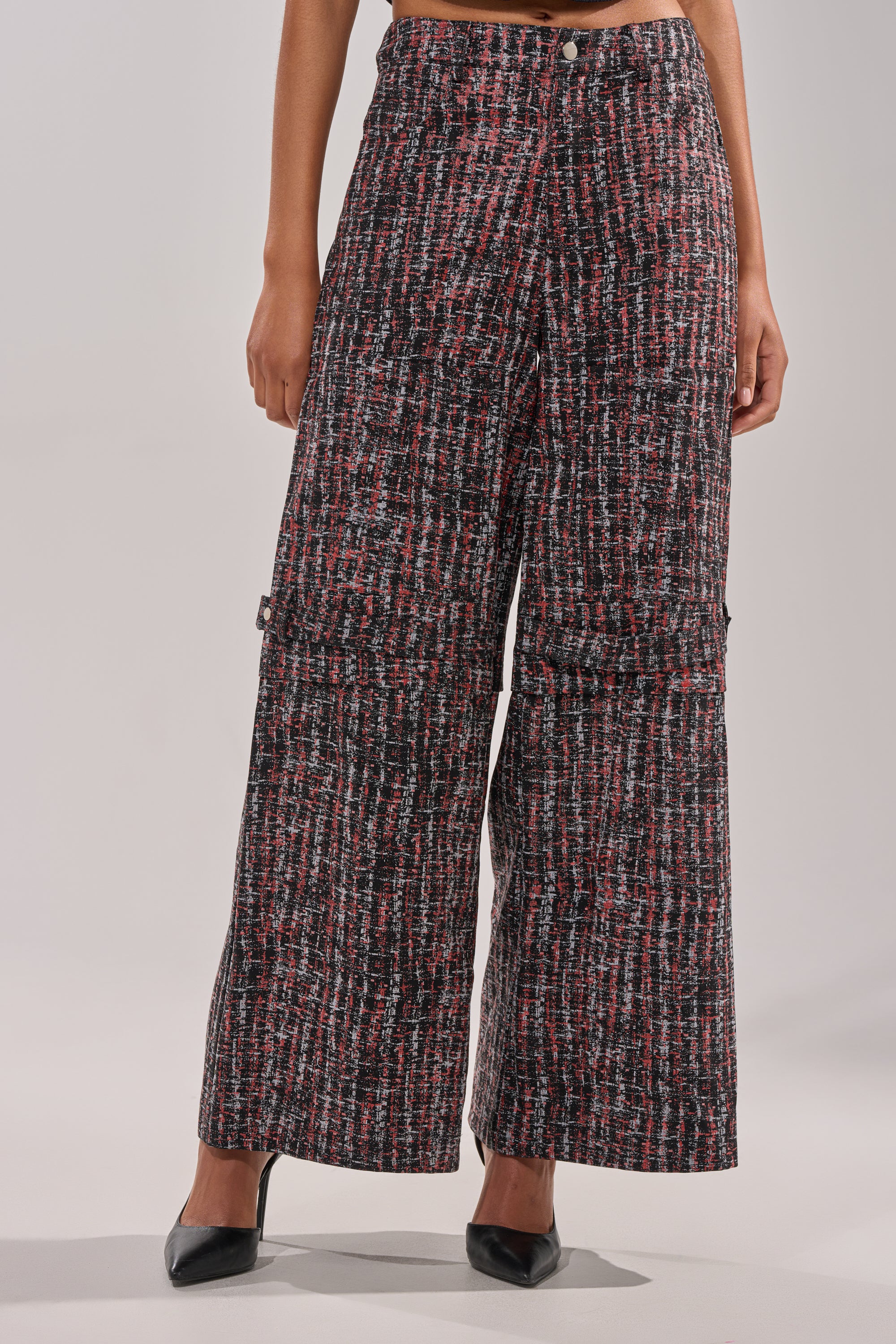 A person wears the WORK IT FAUX LEATHER PLAID TROUSER—high-rise, wide-leg, with a red, black, and white textured plaid—paired with black pointed-toe heels. The image is cropped from the waist down. 2