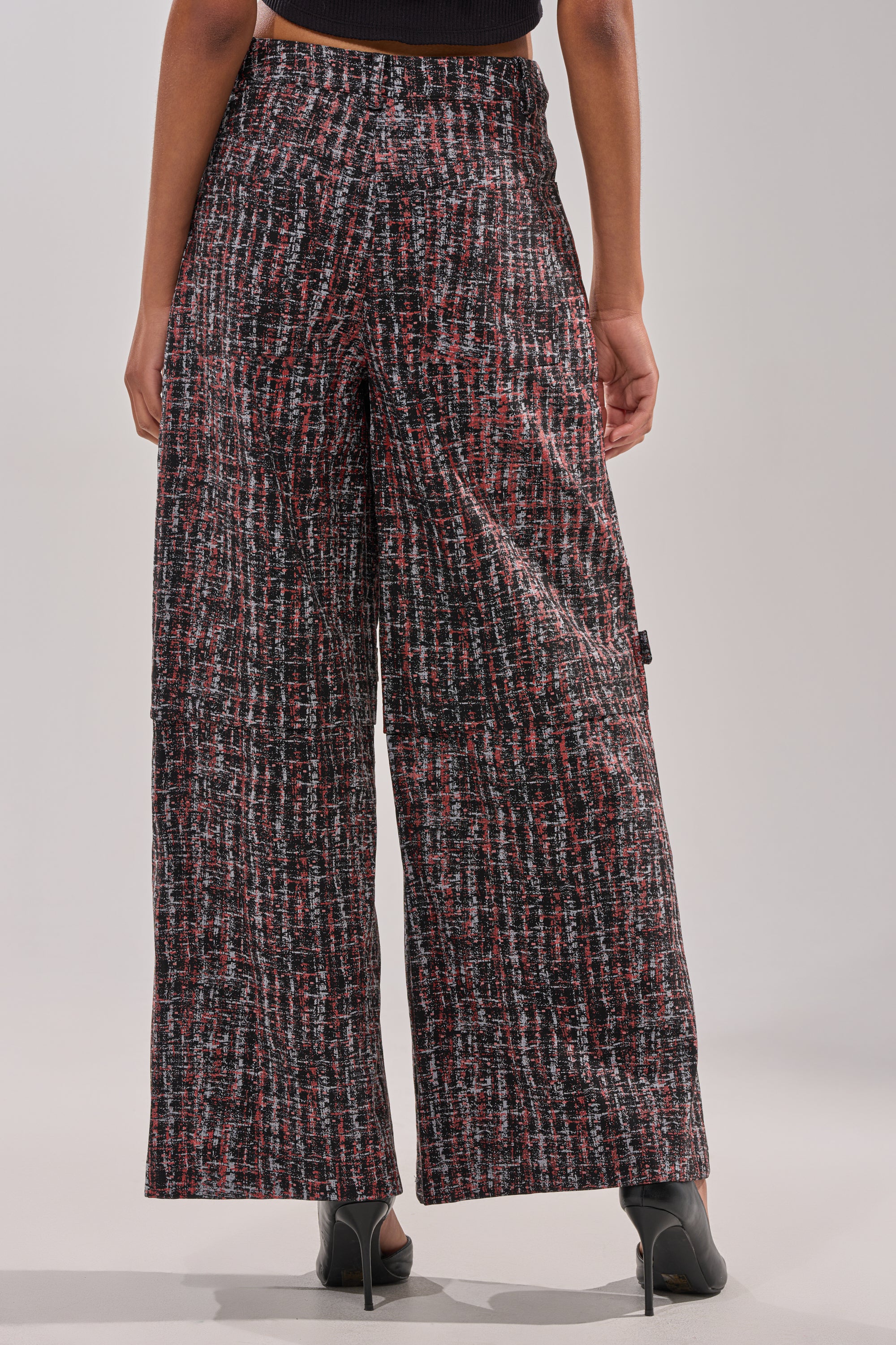 A person is shown from the back wearing the WORK IT FAUX LEATHER PLAID TROUSER, which features a high-rise, wide-leg fit with a red, black, and white plaid pattern, reaching the ankles and styled with black heeled shoes for a chic look. 4