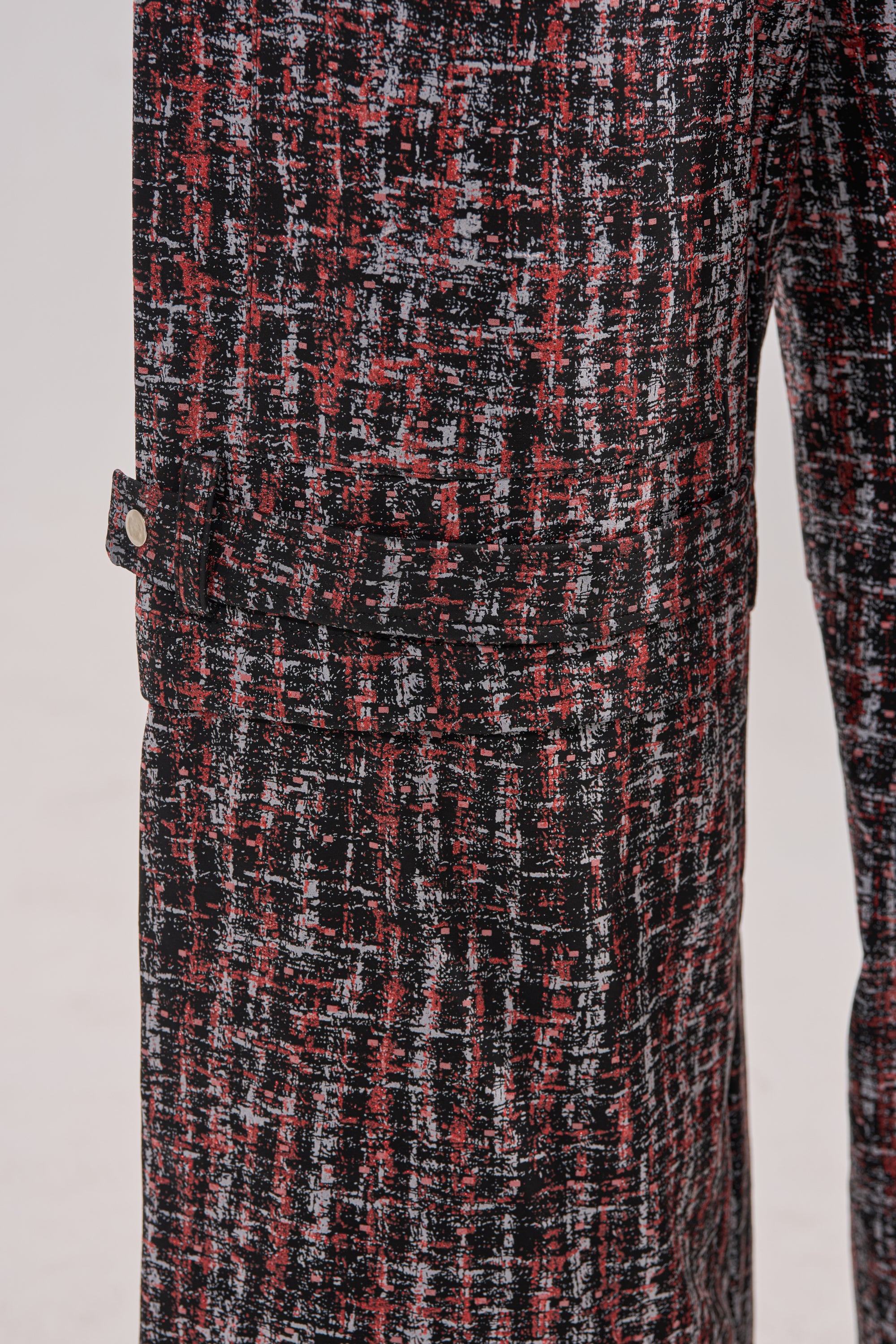 Close-up of the WORK IT FAUX LEATHER PLAID TROUSER pant leg, showing a textured black, red, and white abstract plaid pattern with a side flap pocket and silver button. The background is light and plain. 7
