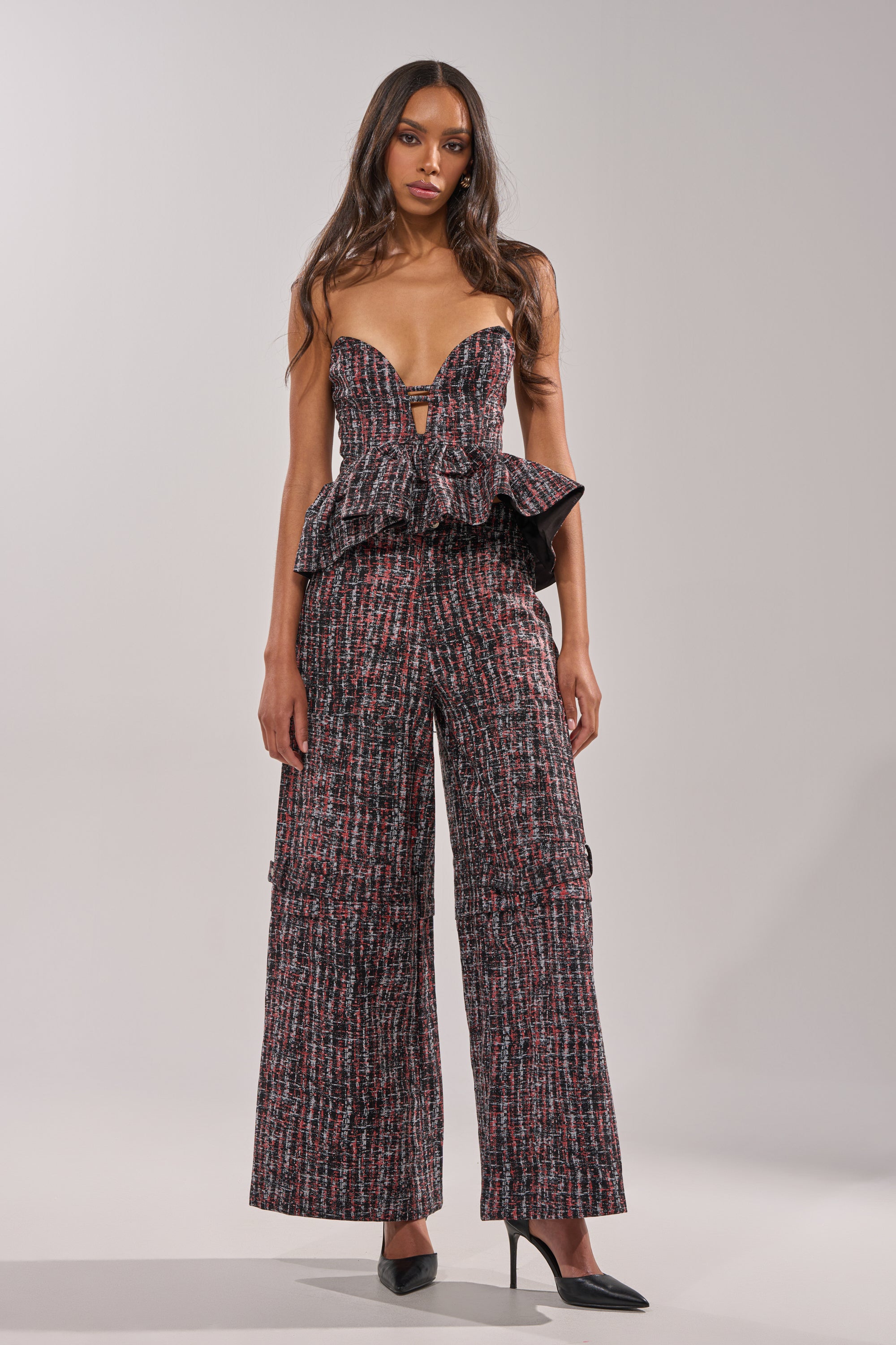 A woman wears the WORK IT FAUX LEATHER PLAID CORSET, featuring a strapless, structured sweetheart neckline and multicolored plaid design, styled with matching wide-leg pants and black pointed heels against a light gray background. 5