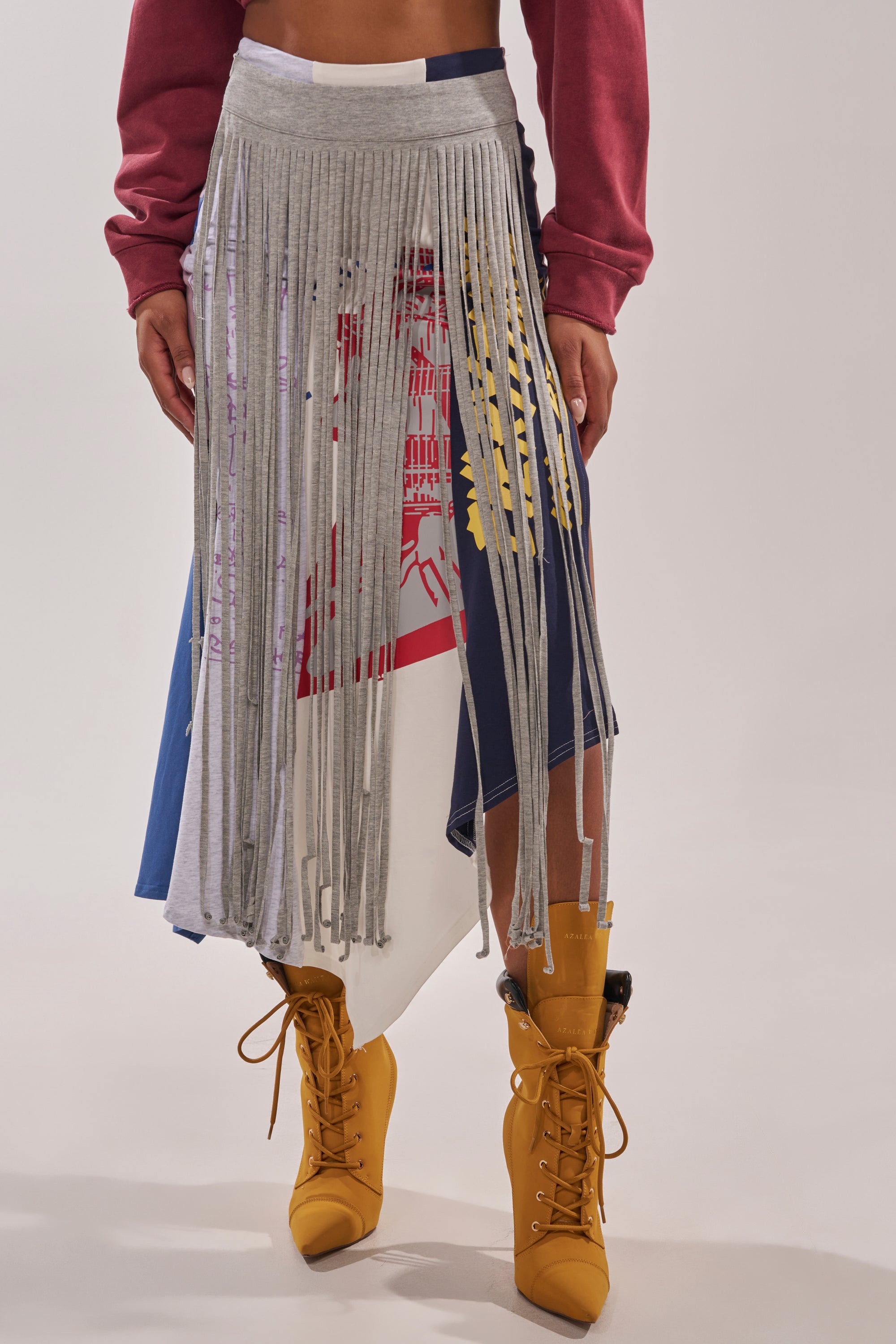 Someone wearing the STRESSED AND DISTRESSED MIDI SKIRT layered under a gray, fringed overskirt, teamed with mustard yellow lace-up boots and a maroon long-sleeved top. 1