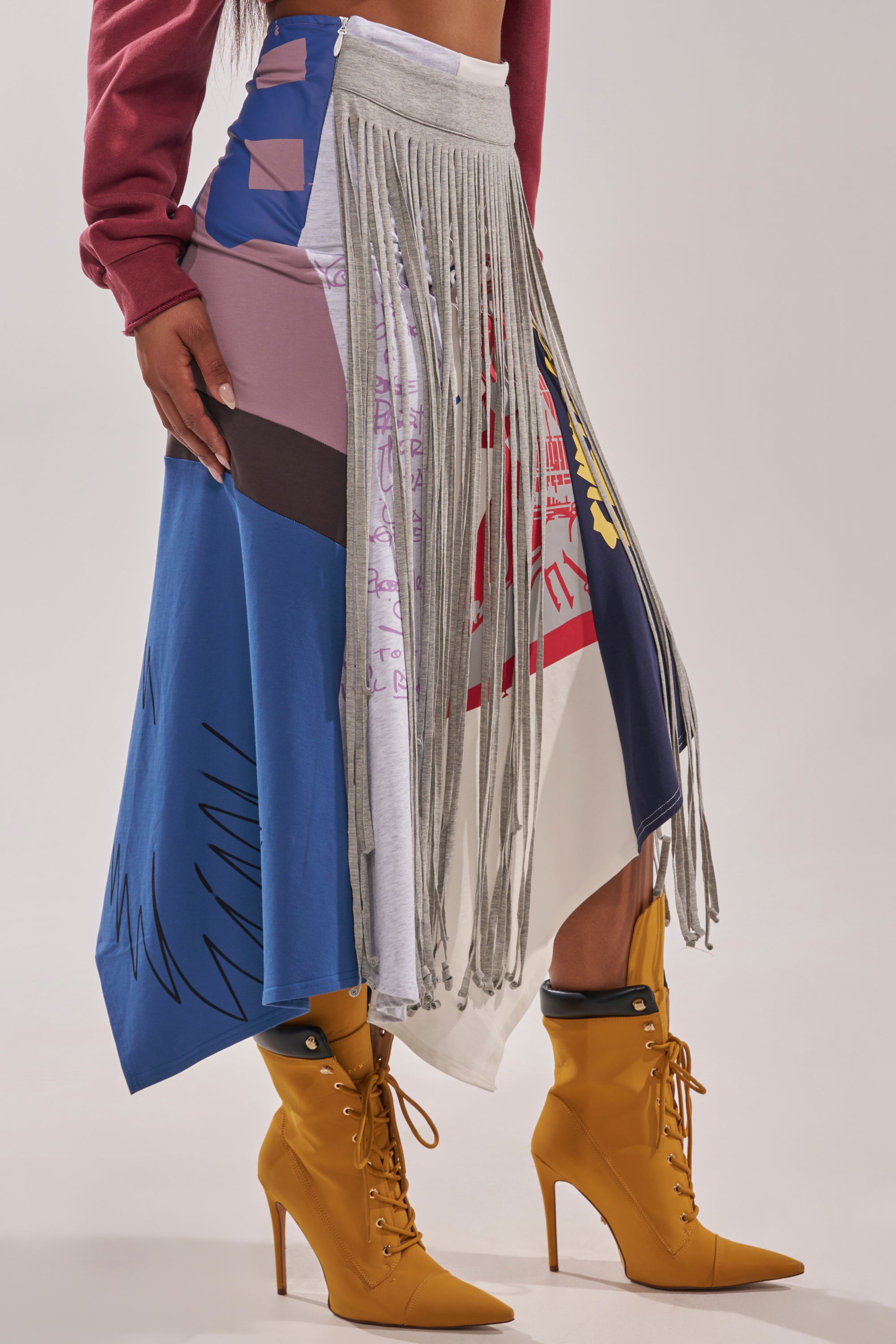 Someone wearing the STRESSED AND DISTRESSED MIDI SKIRT, a maroon long-sleeve top, and yellow lace-up high-heeled boots stands against a plain background. 3