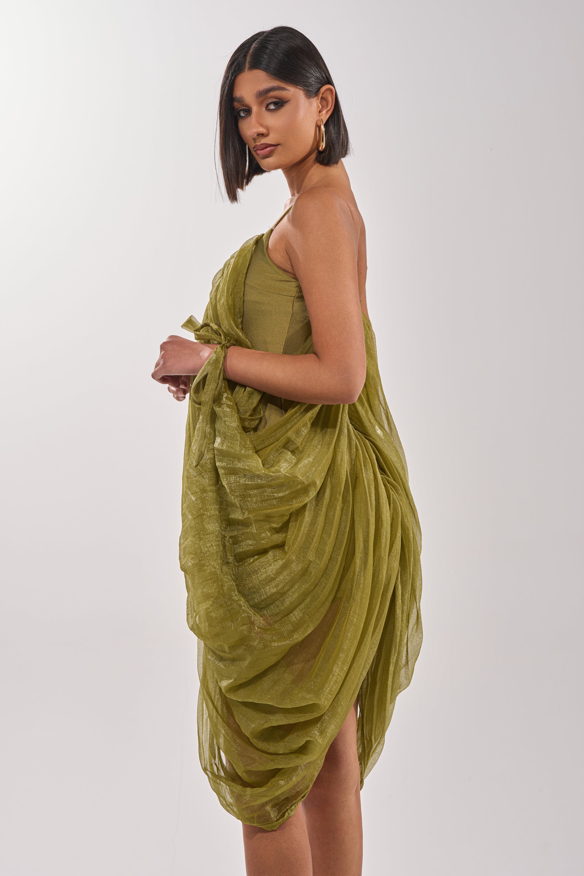 A woman exudes timeless style in the VIVA LA VIDA MESH DRESS, its elegant draping and olive hue perfectly complementing her graceful silhouette. 4