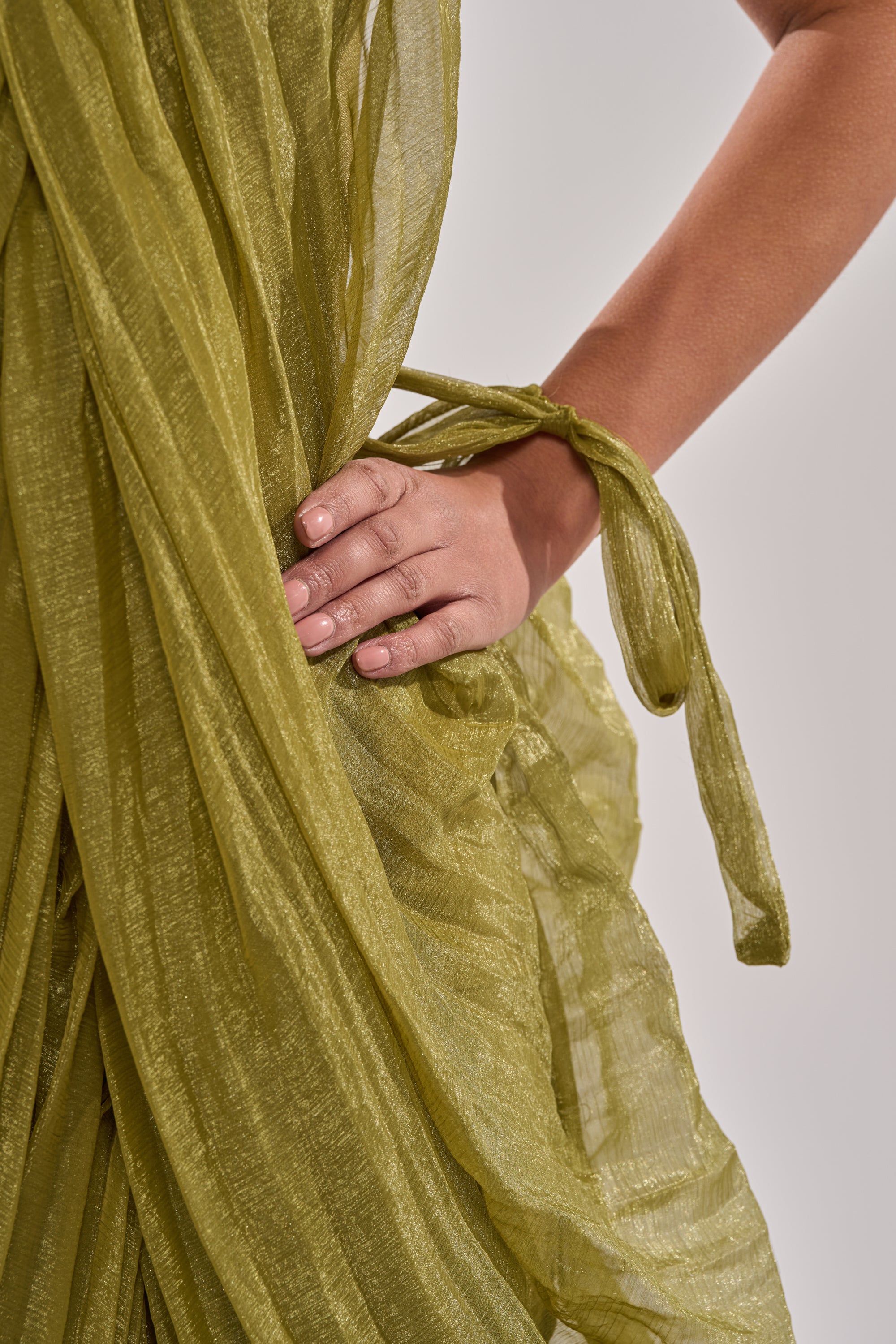 A close-up of a hand holding the pleated, sheer green fabric of the VIVA LA VIDA MESH DRESS, featuring a fabric tie around the wrist against a neutral background. 8